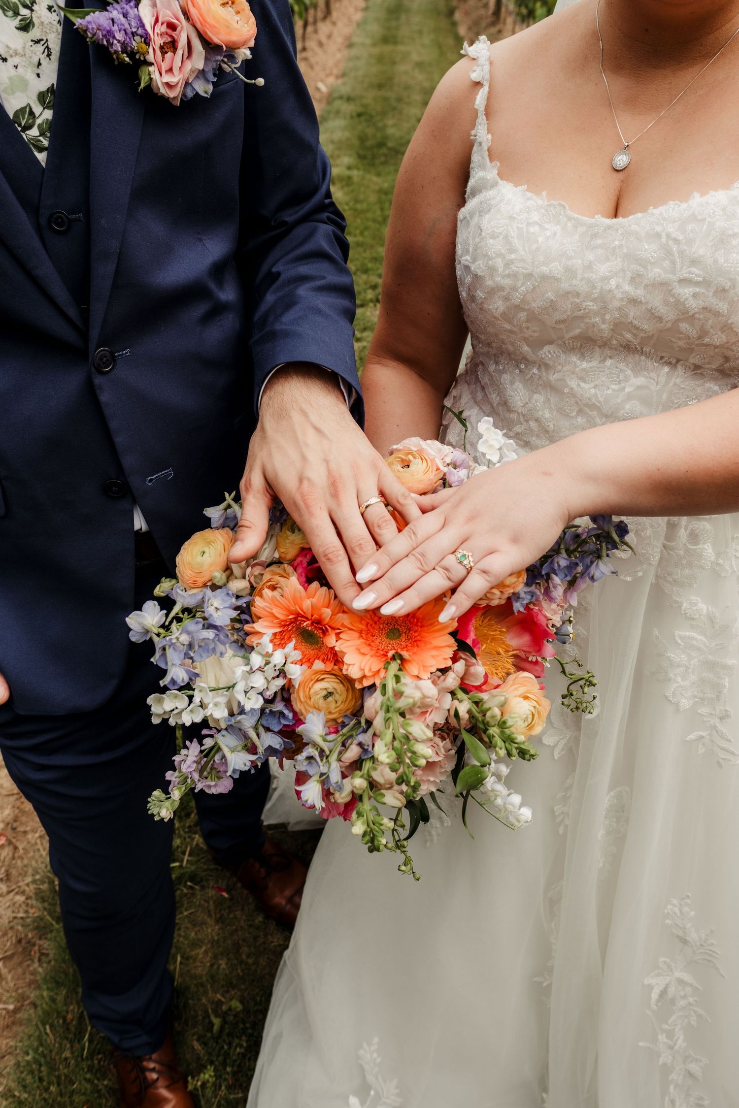 Bride and groom display wedding rings over a vibrant orange and purple bridal bouquet.
