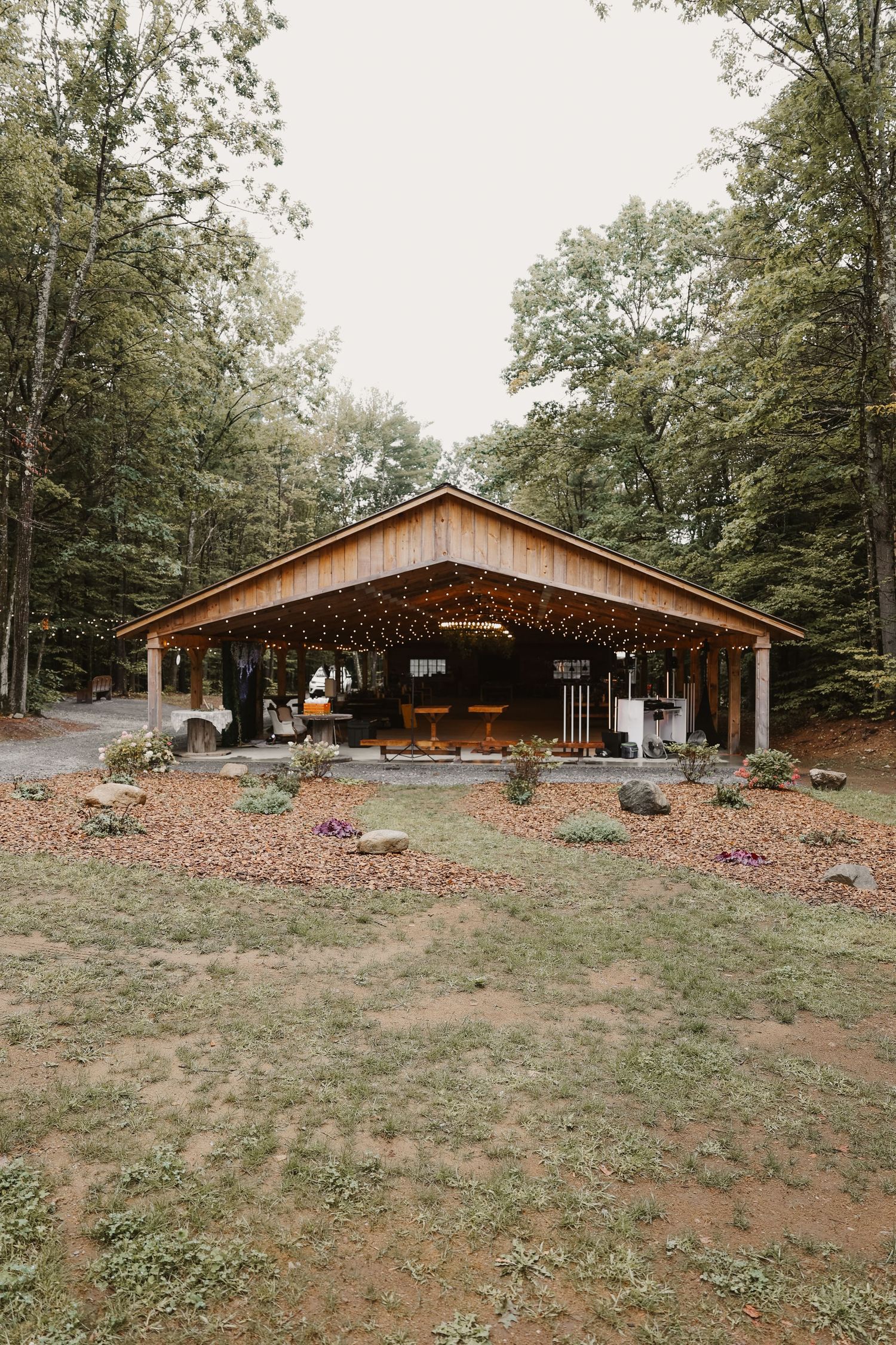 Open-air wooden wedding pavilion adorned with string lights surrounded by tall forest trees.