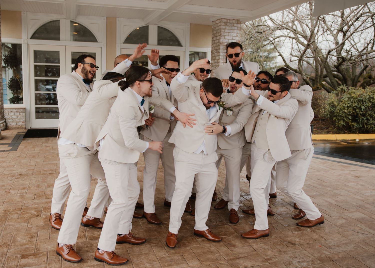A groom celebrates joyfully with his groomsmen all dressed in matching white suits.