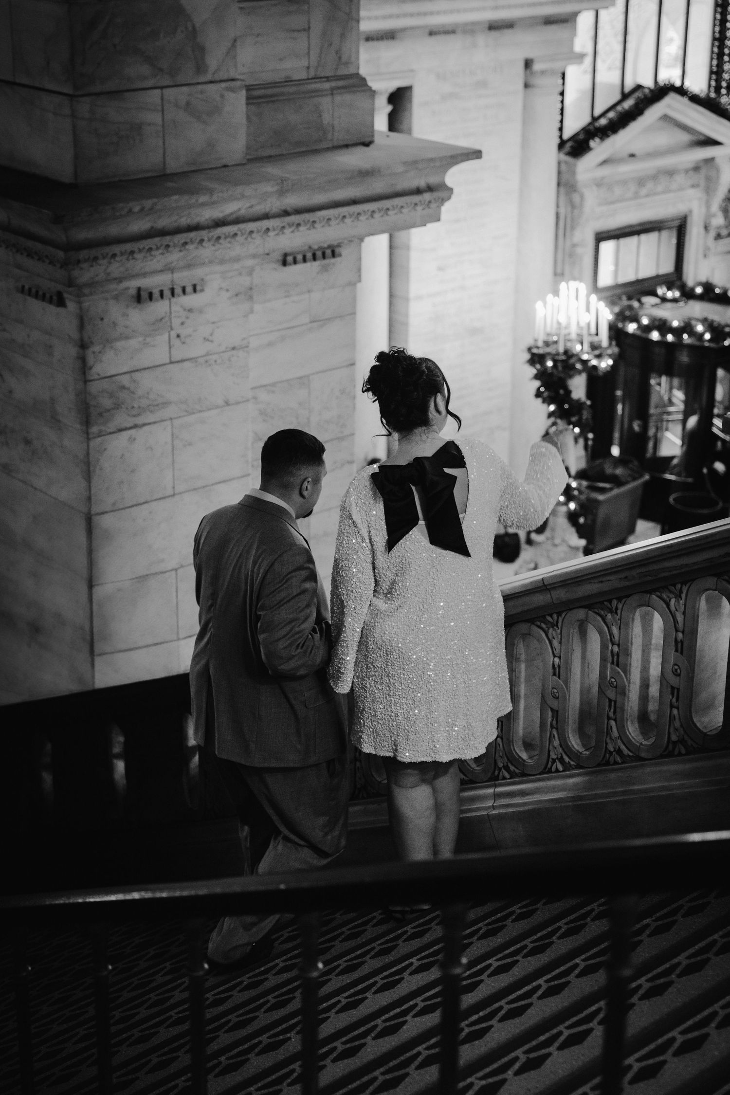 Black and white overhead shot of couple holding hands ascending grand staircase in elegant venue.