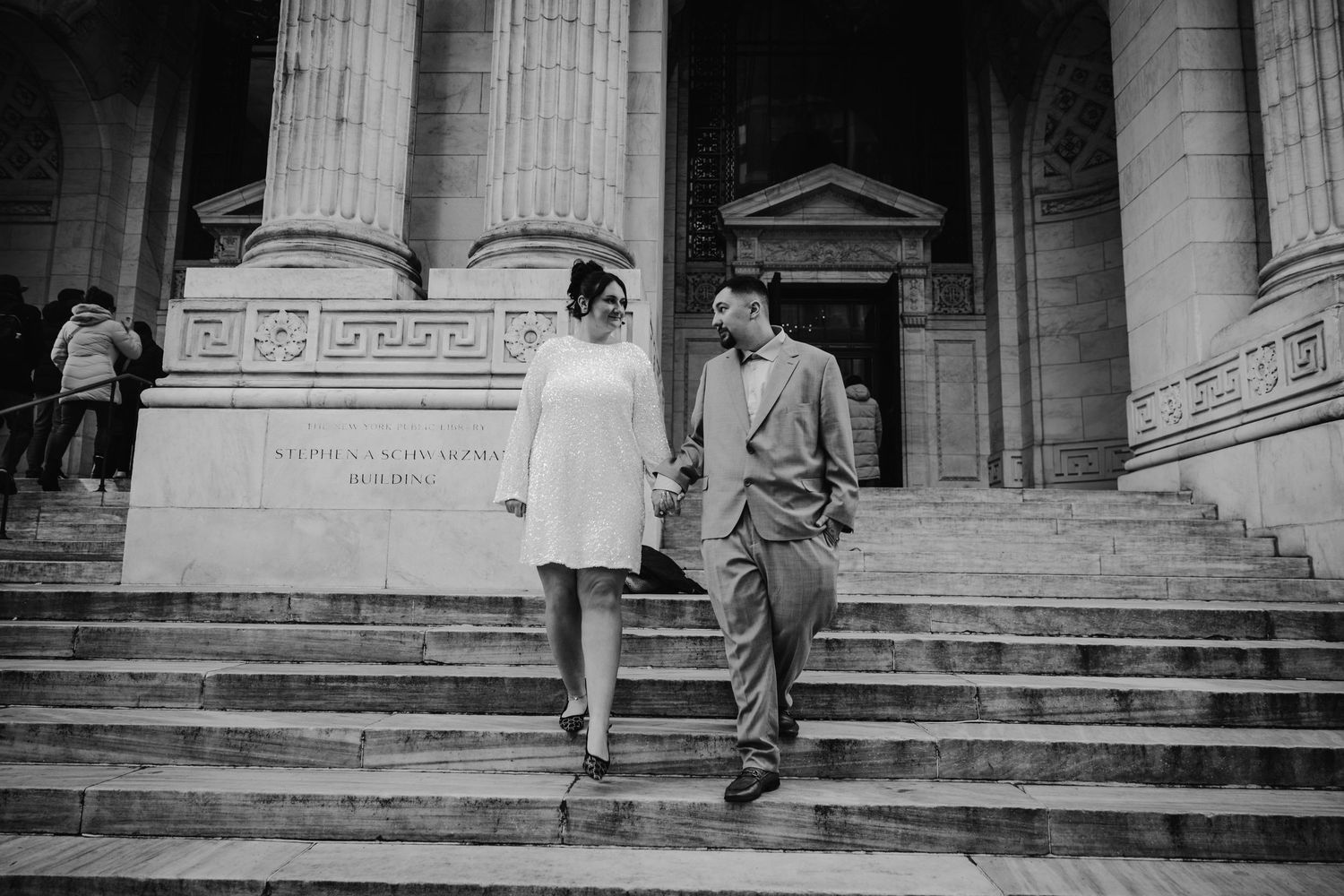 Black and white photo of couple holding hands on steps of grand columned building.