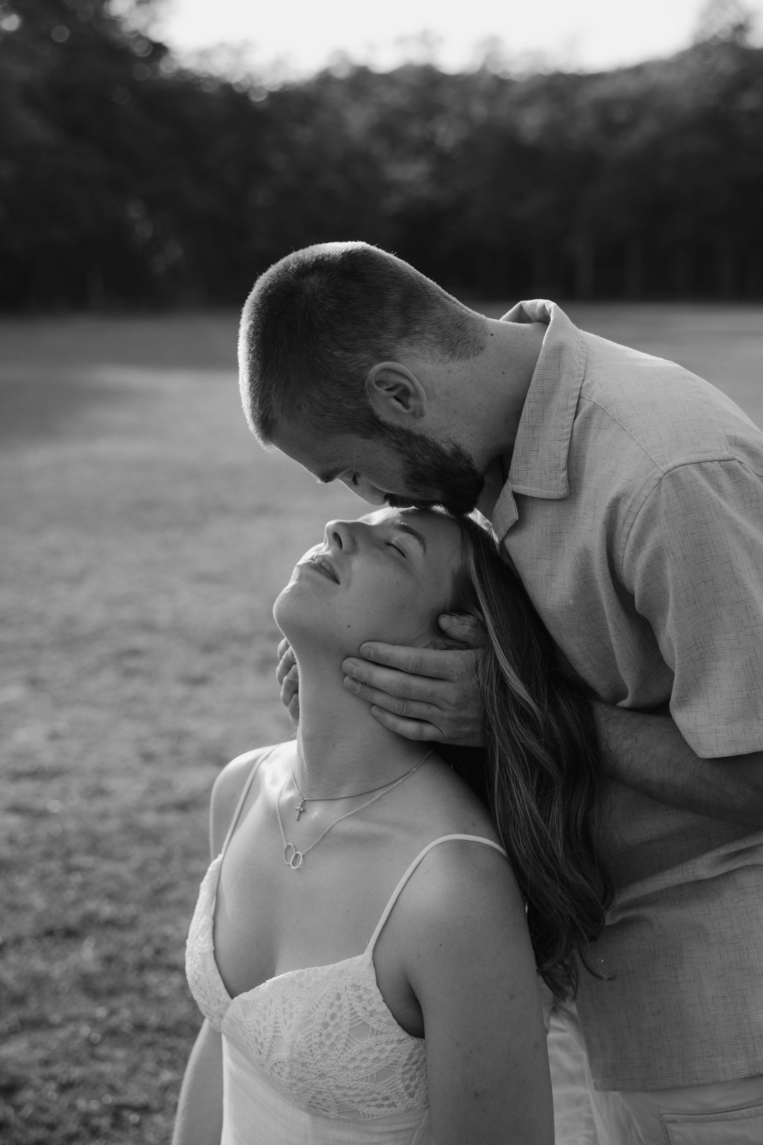 Black and white photo of a man tenderly kissing a woman on the forehead while cradling her face.