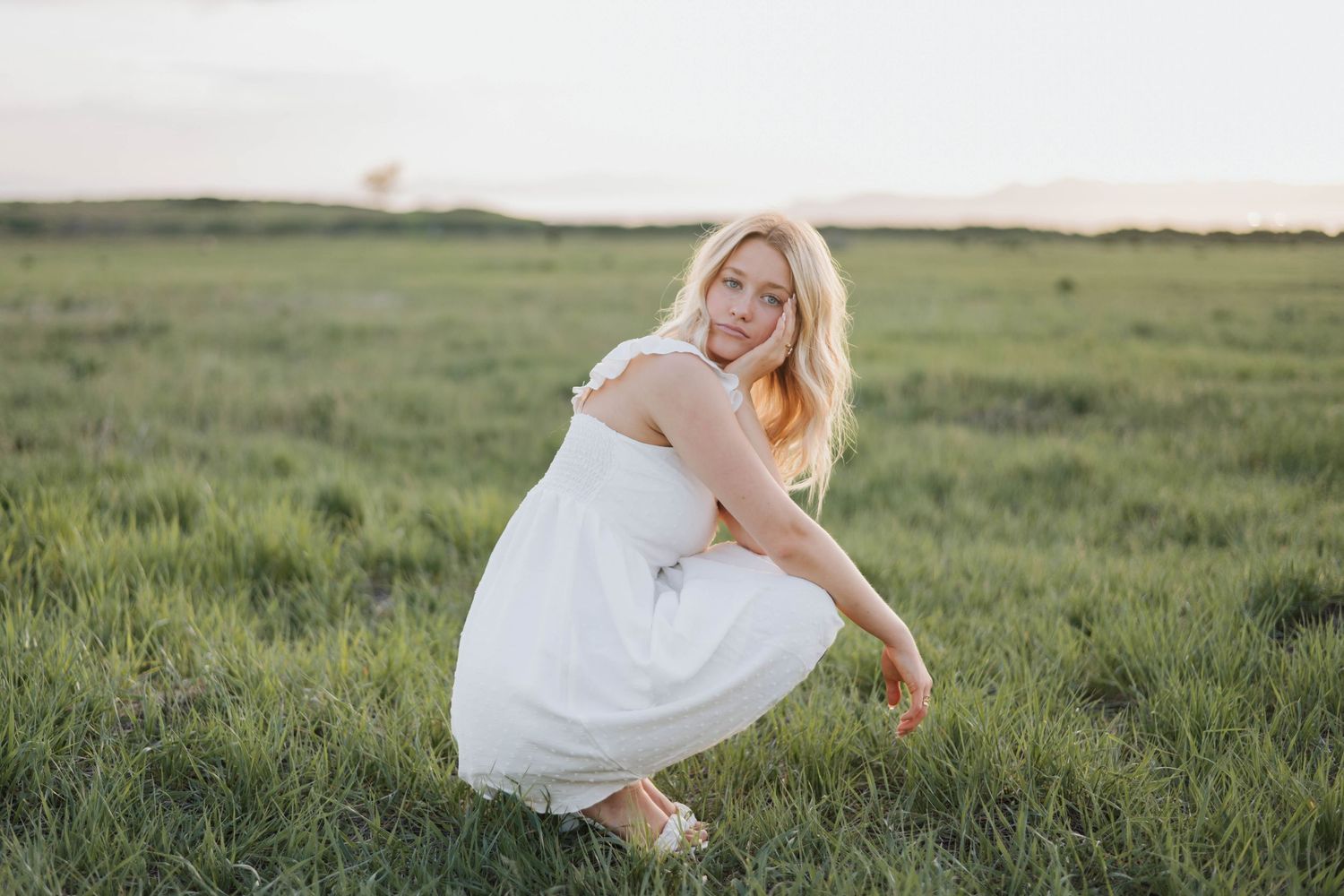 Natural light senior portrait of a young woman in an open field at sunset.