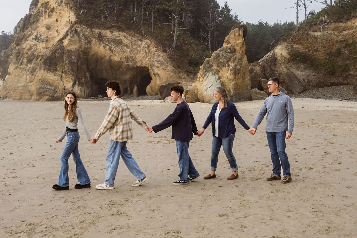 Family of five walking hand in hand along the Oregon coast during a natural light family photography session.