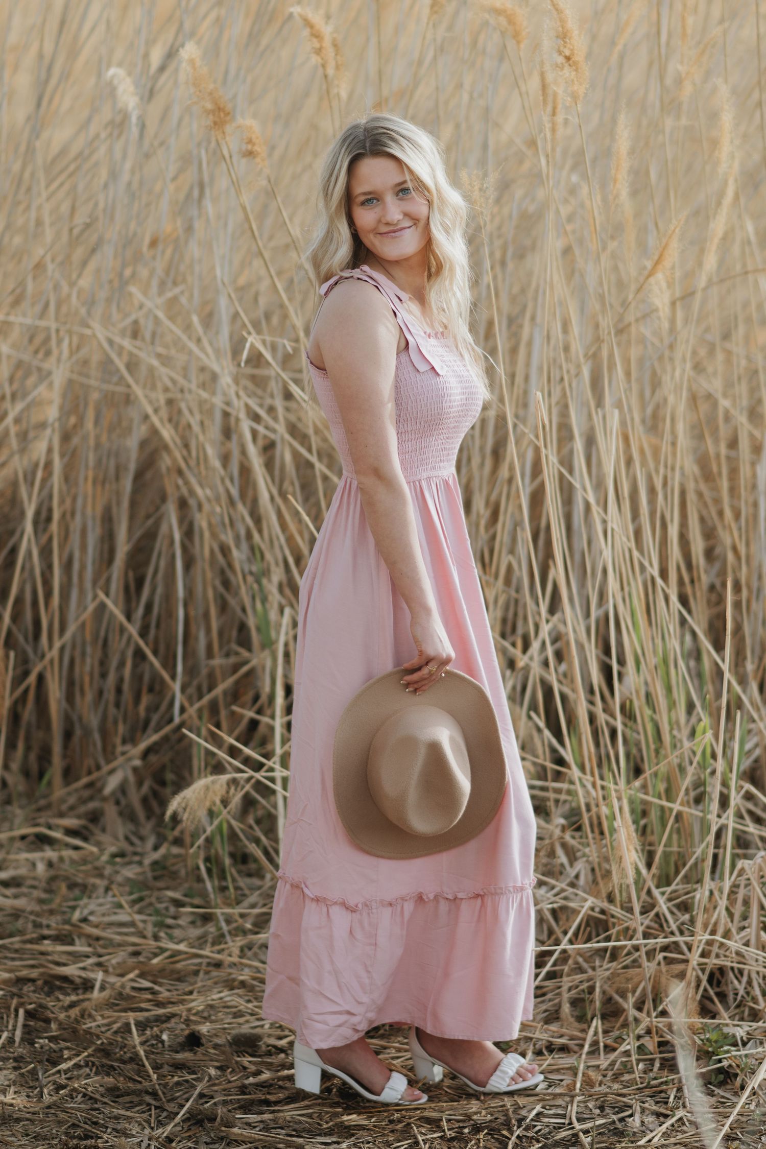 Natural light senior portrait featuring a young woman in a golden field with a wide-brim hat.
