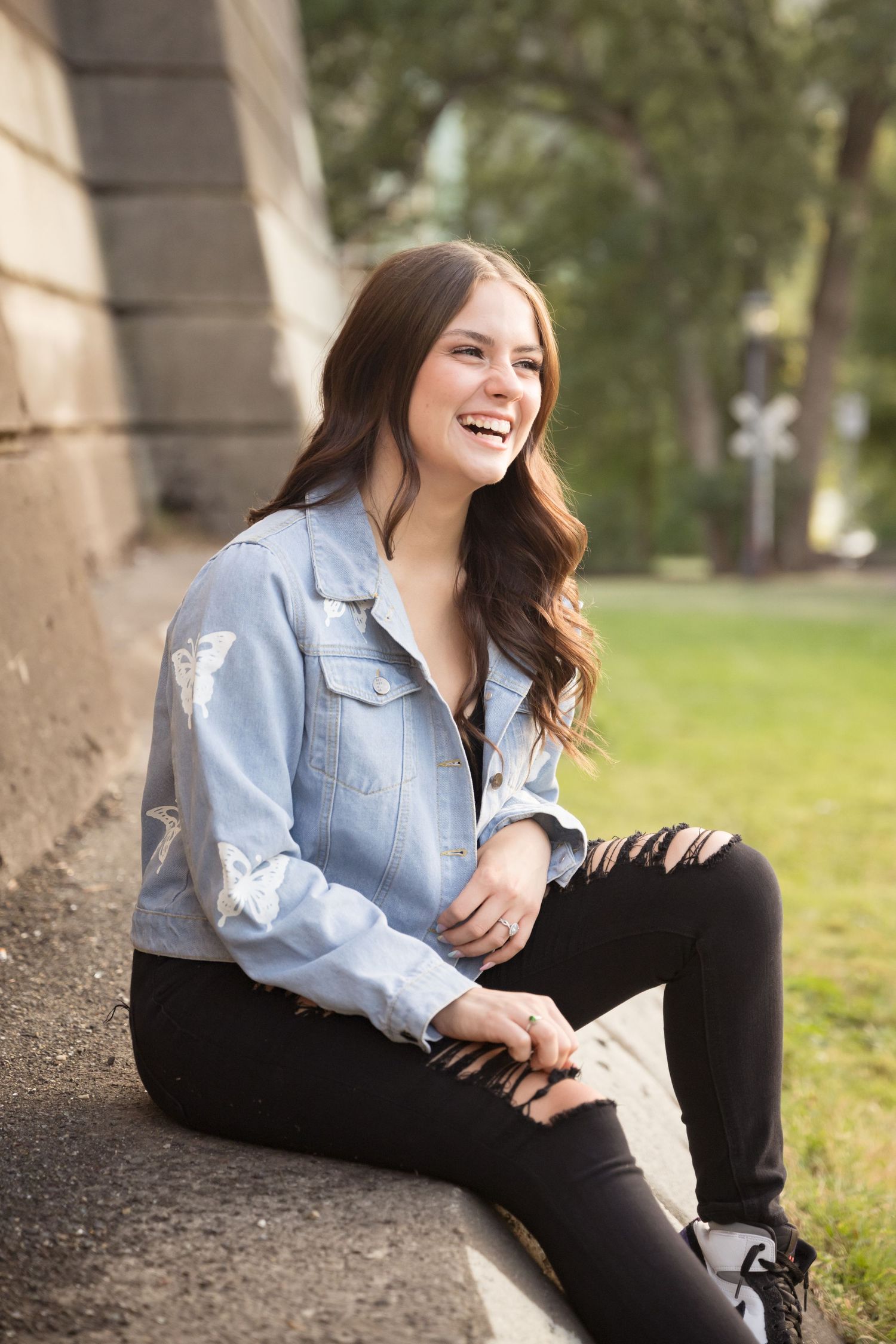 High school senior girl sitting against a stone wall during a natural light outdoor senior portrait session in Utah.