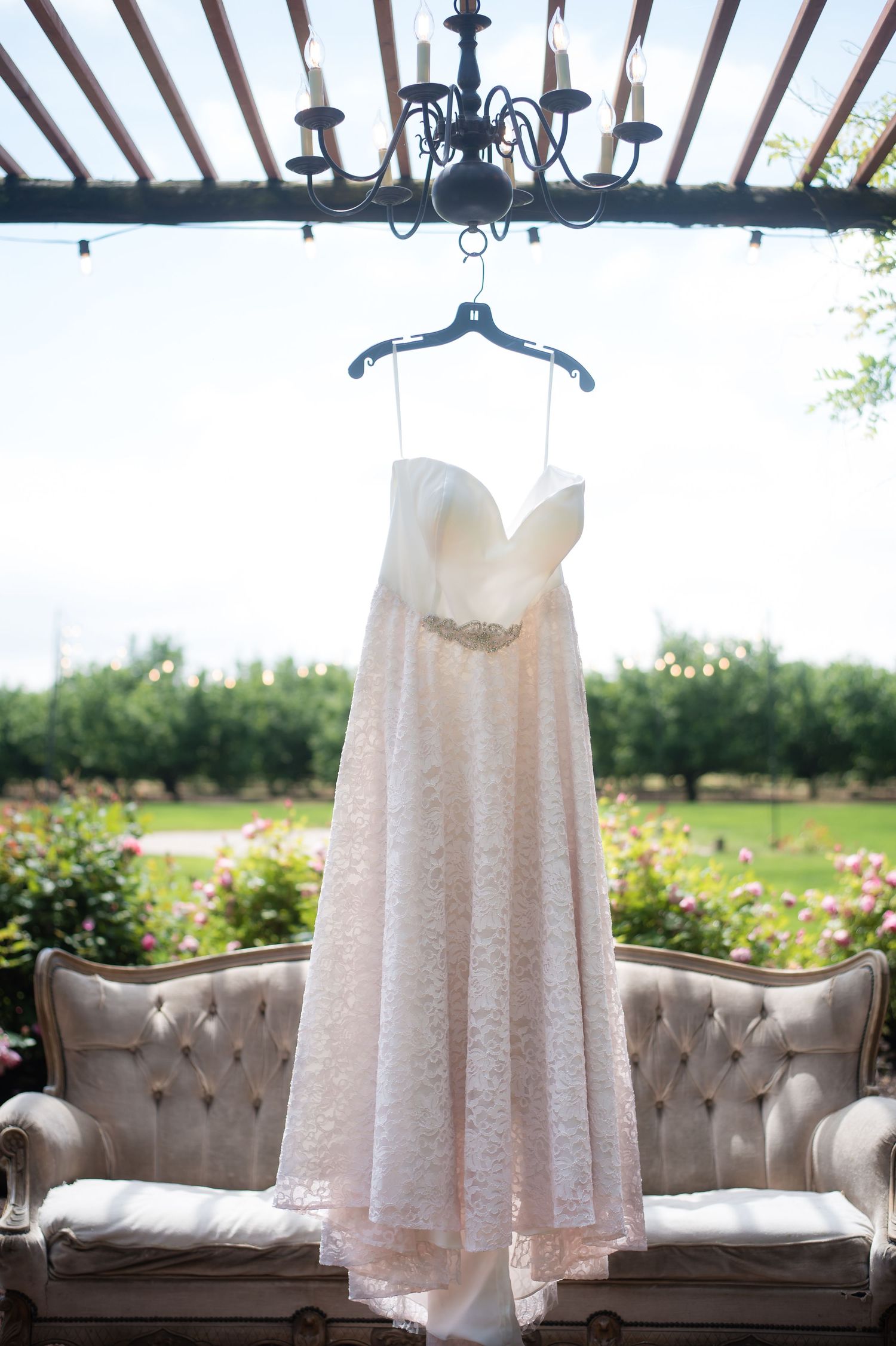 Elegant wedding dress hanging beneath a wooden pergola before the bride gets ready.