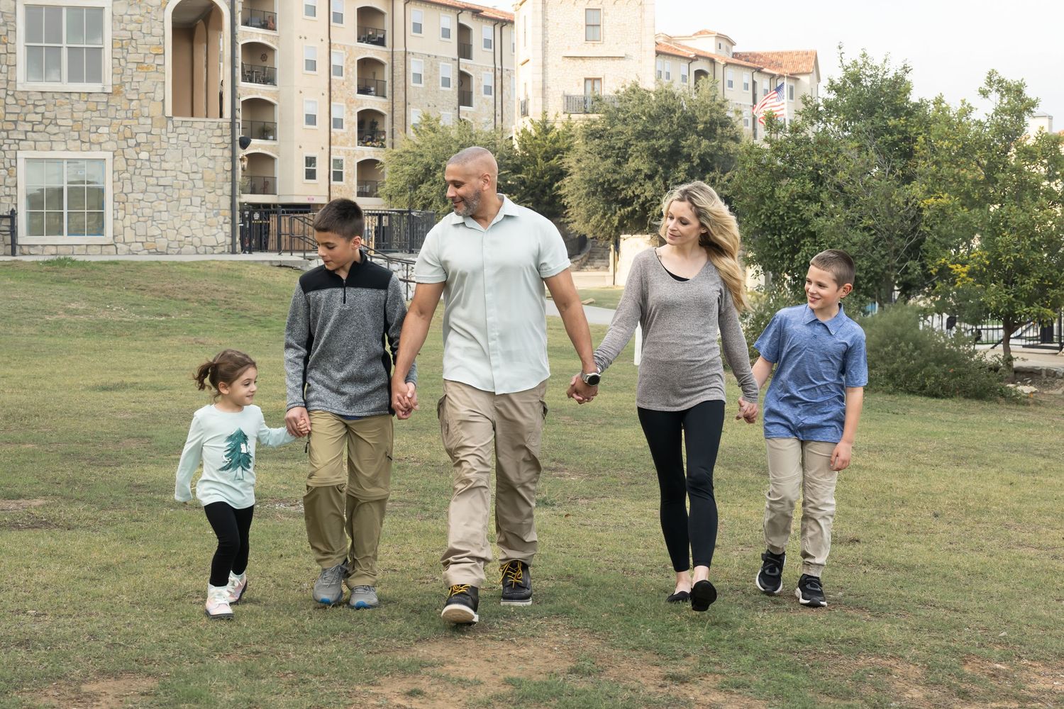 Family walking hand in hand through a neighborhood park during an outdoor lifestyle family photography session.