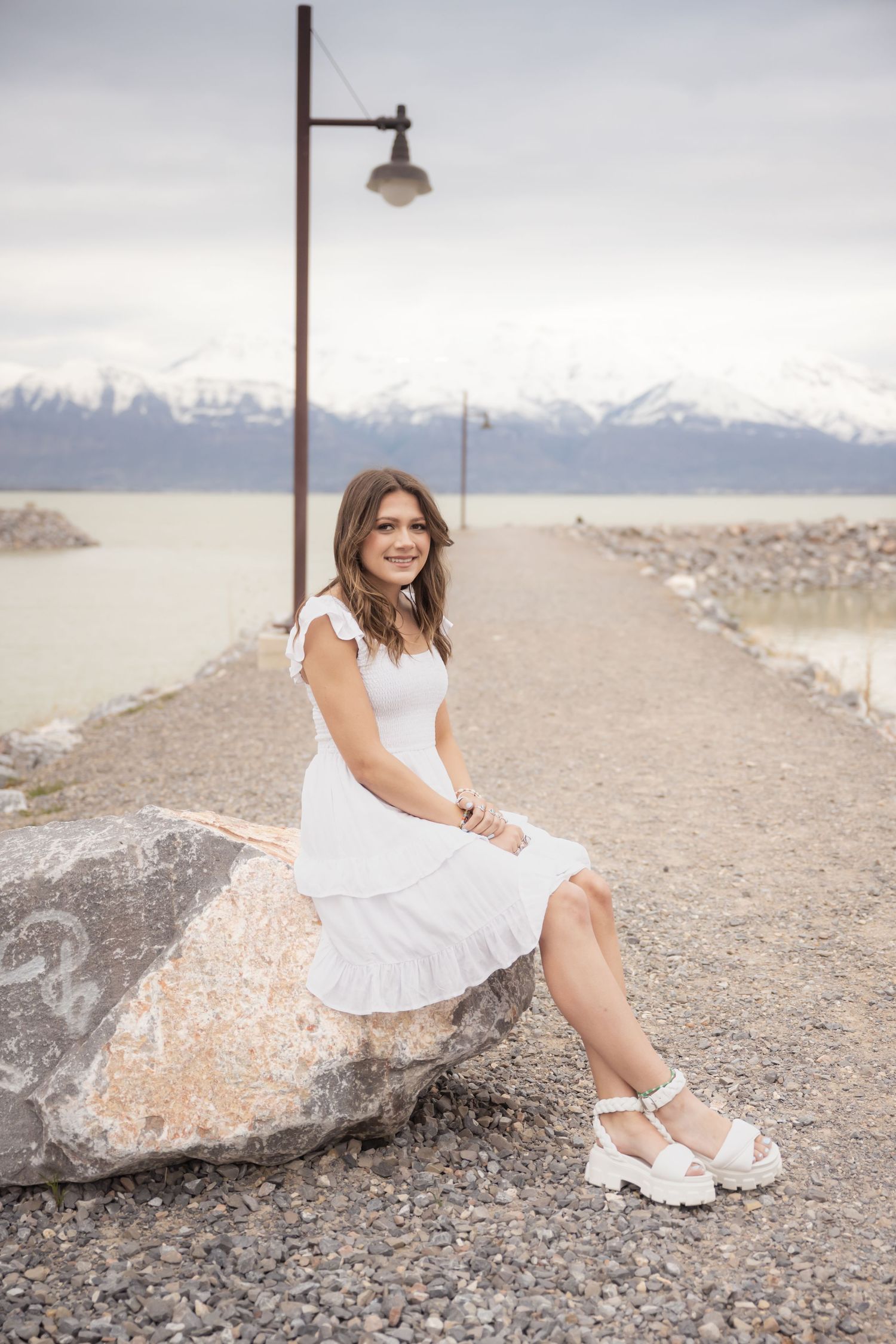 High school senior in a white dress posing along the Utah Lake shoreline during a scenic Utah senior photography session.