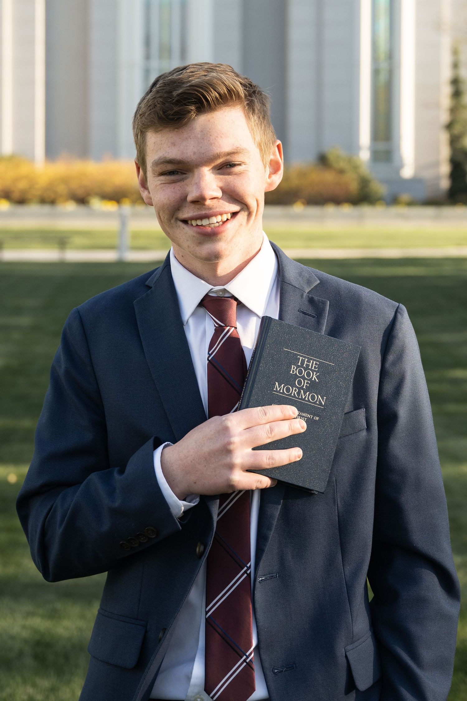 Smiling LDS missionary portrait holding a Book of Mormon before departing to serve a mission.