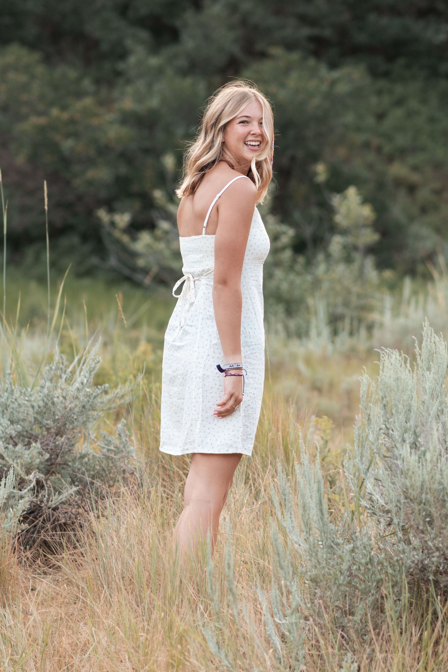 Natural light senior portrait featuring a young woman surrounded by tall grass at golden hour.