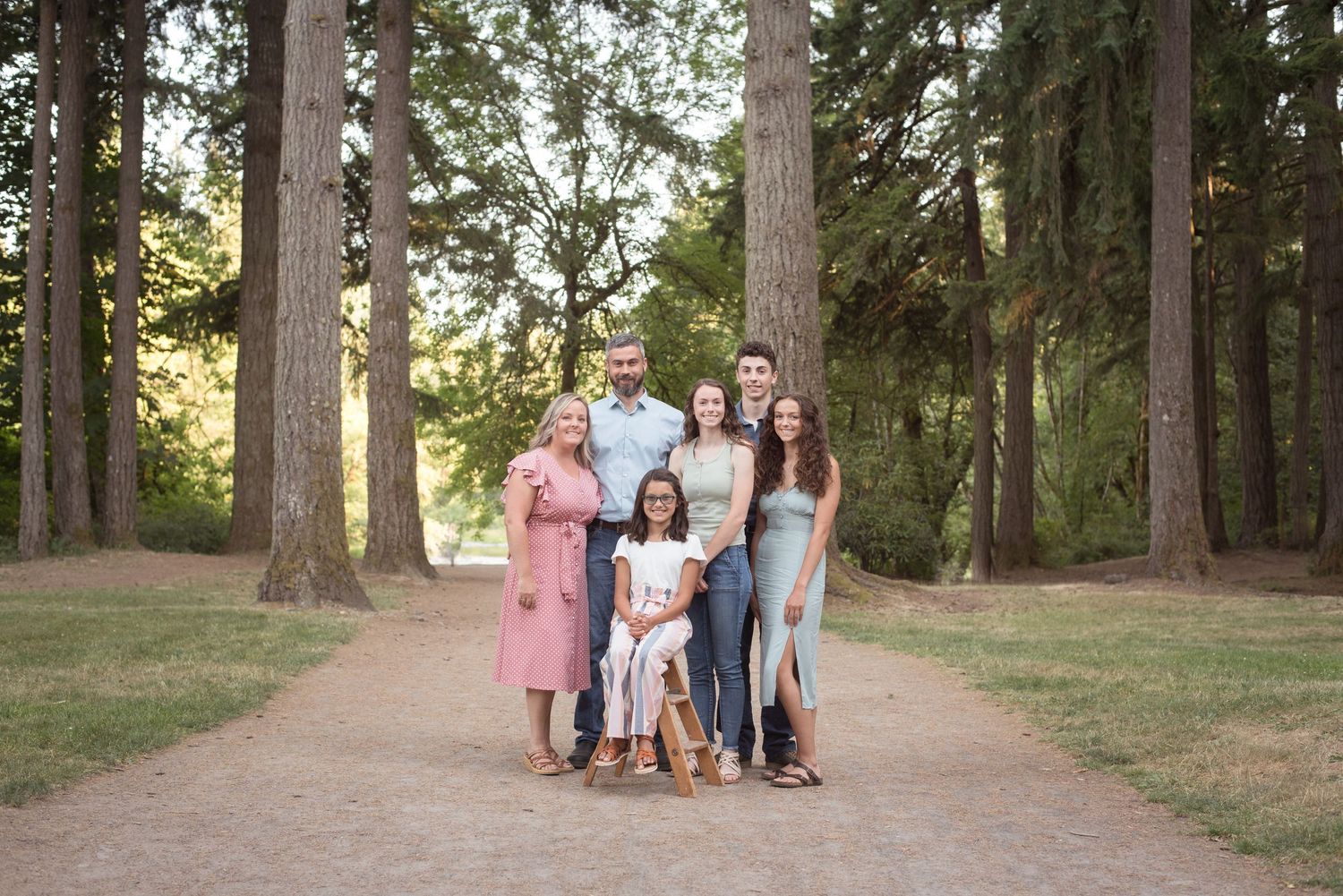Family of five standing together beneath towering pine trees during a timeless outdoor portrait session in Washington.