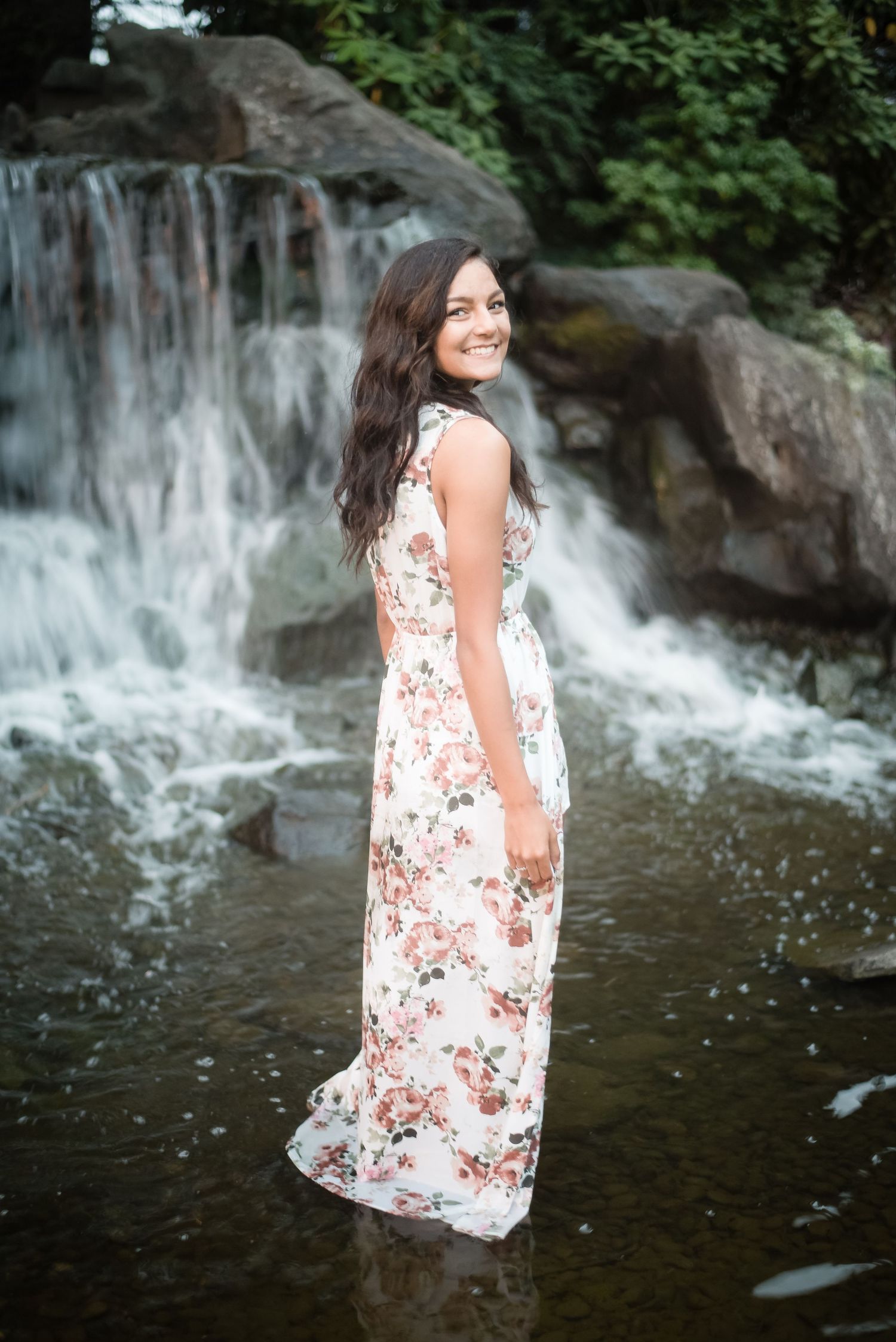 Young woman standing beside a waterfall during an outdoor portrait photography session in Washington.