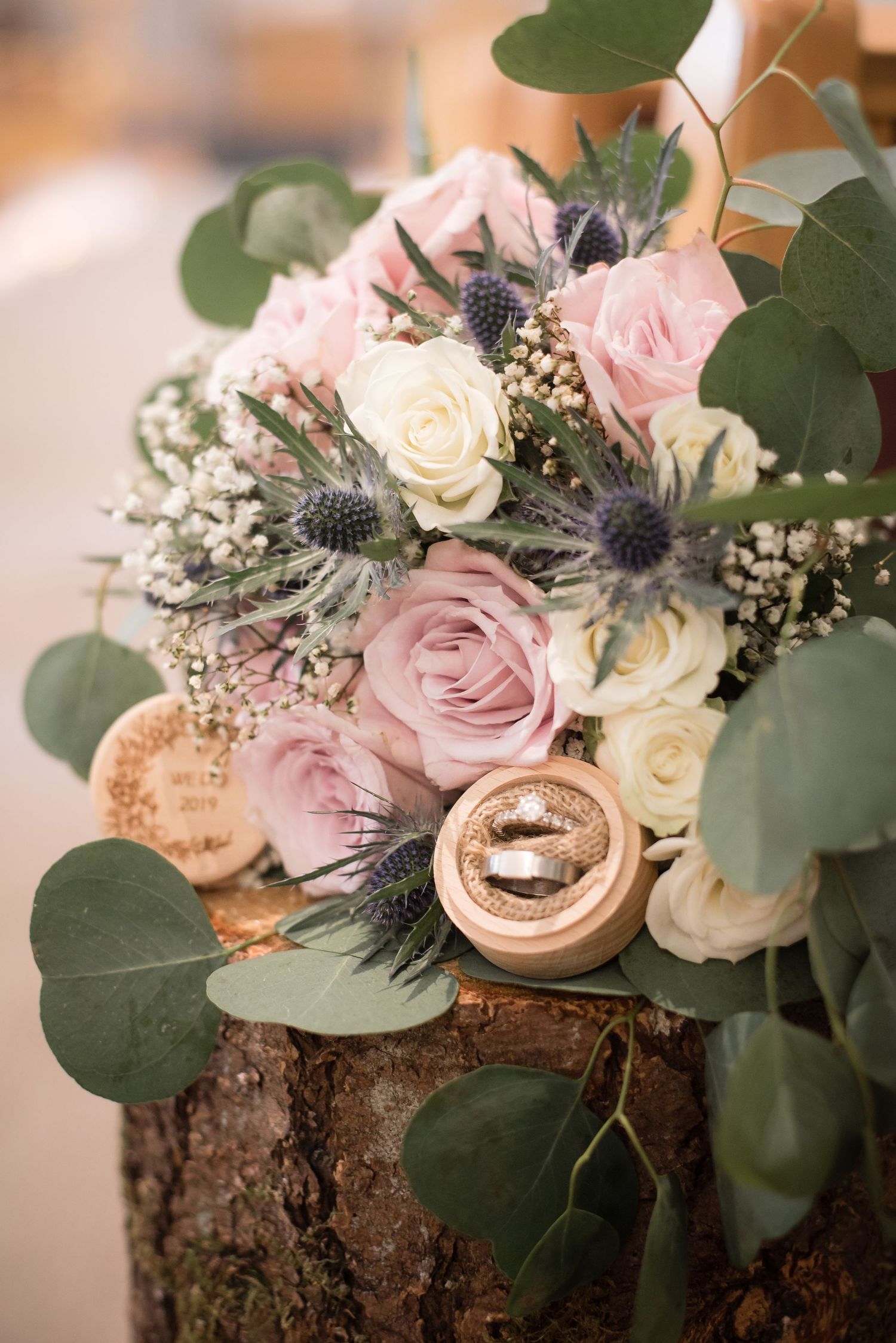 Wedding detail photograph featuring bridal bouquet, wedding rings, and floral arrangements.
