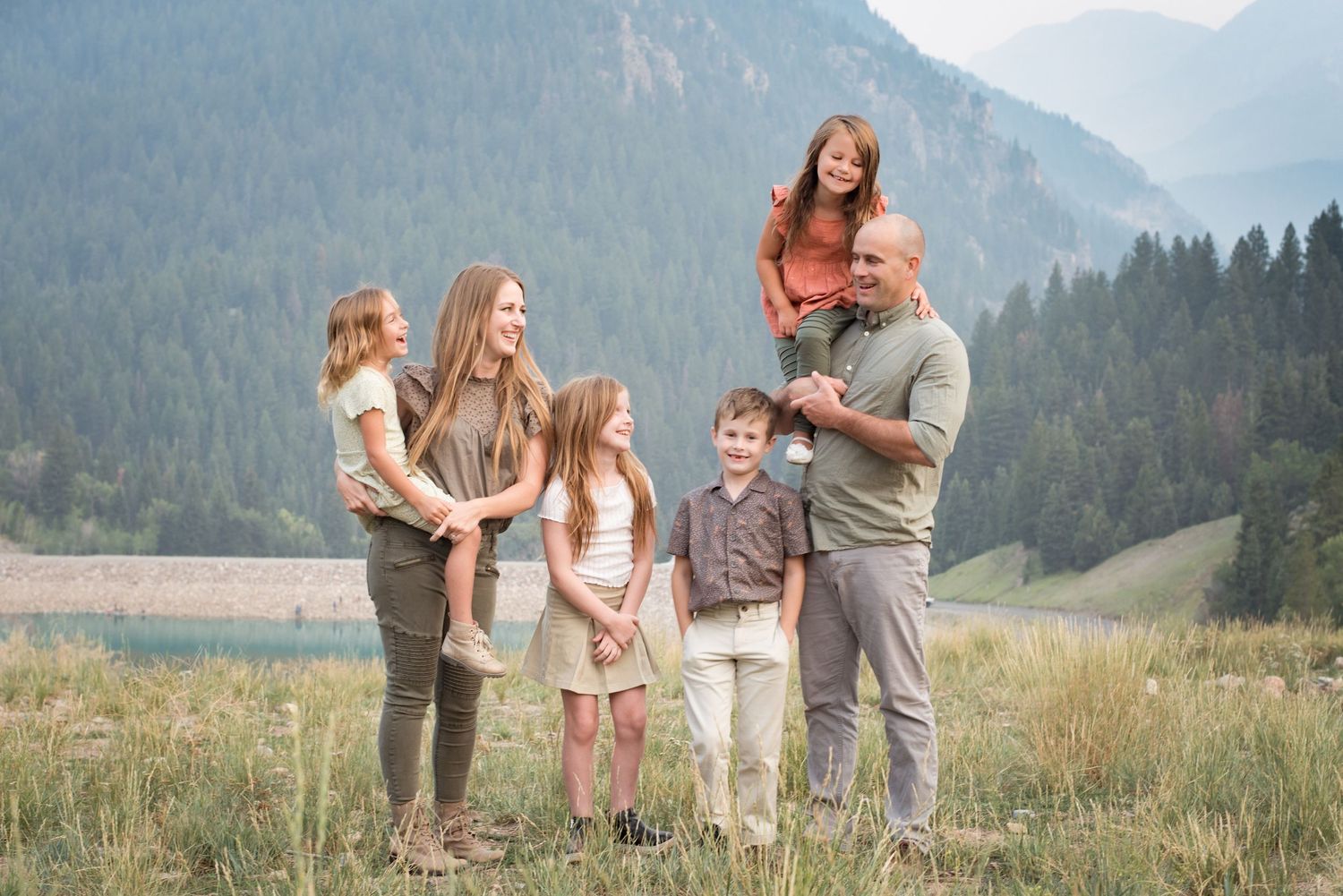 Family of five smiling together during an outdoor family photography session with mountain views in Utah.