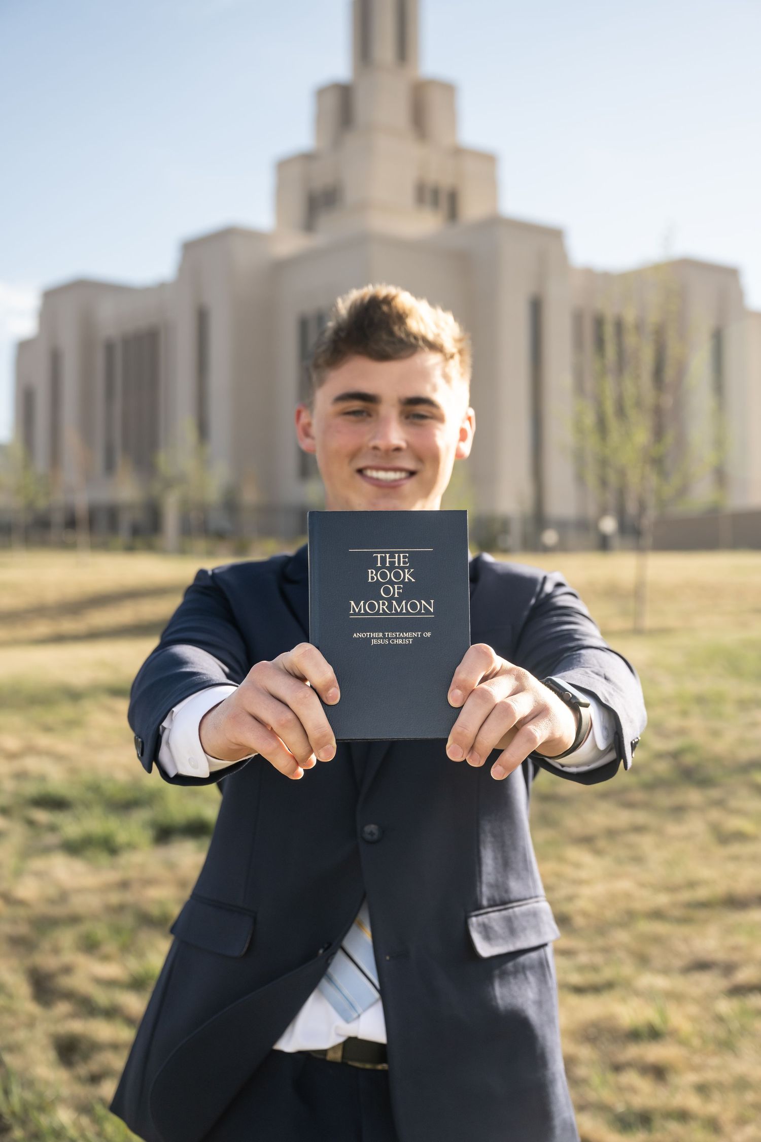 LDS missionary holding a book of mormonl in front of the temple during a farewell photography session in Utah County.