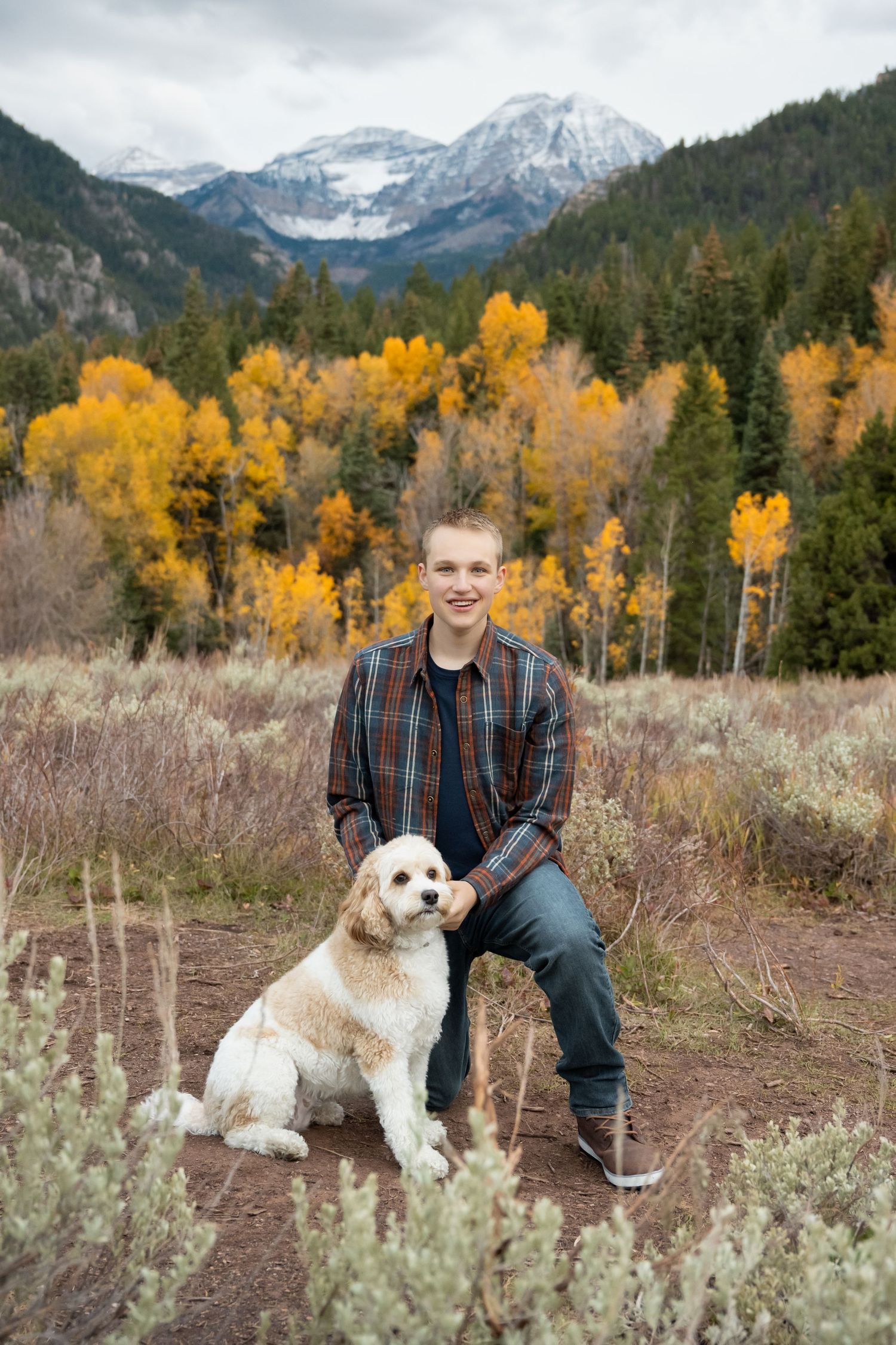 High school senior posing with a Goldendoodle surrounded by colorful fall mountains during a Utah senior photography session.