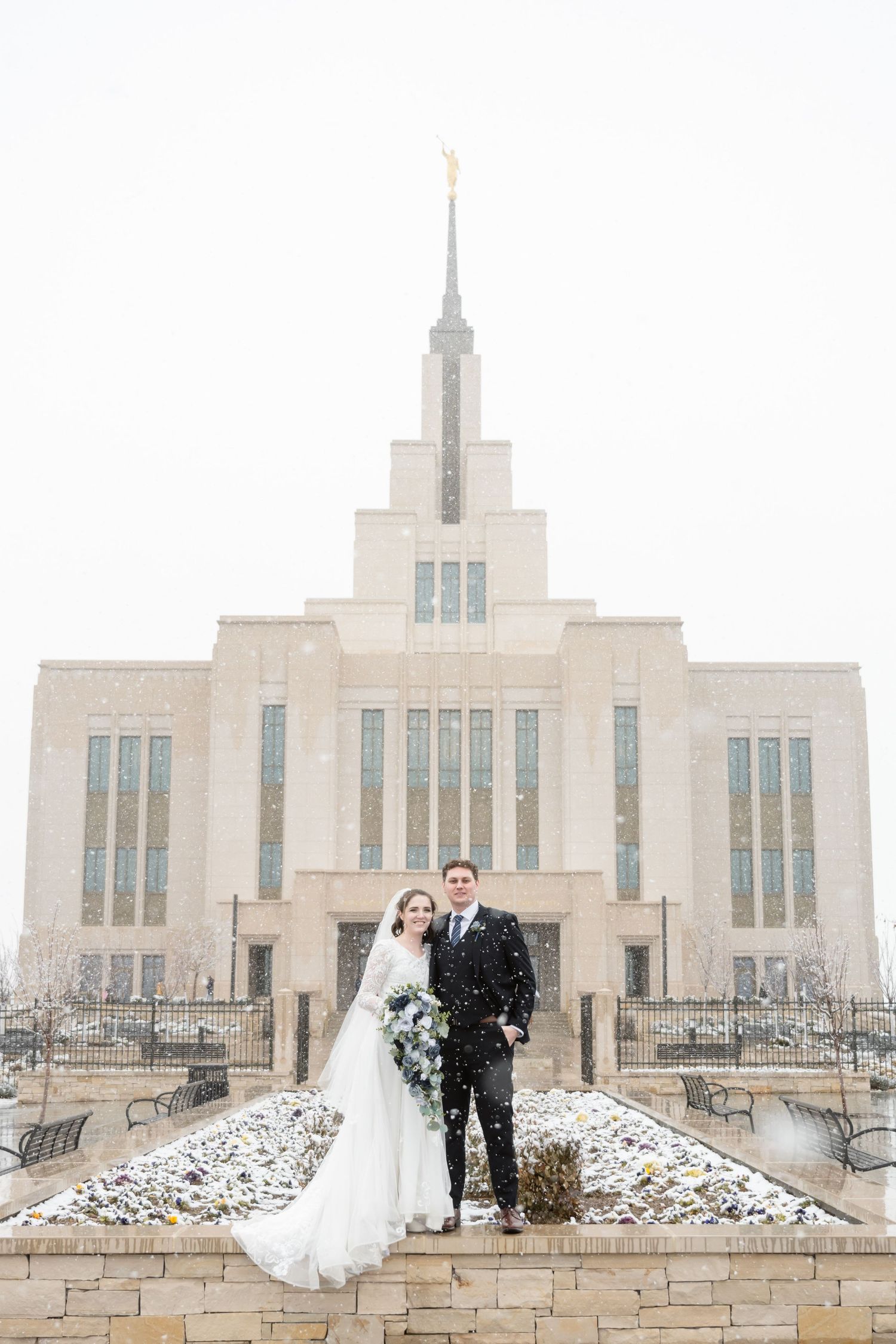 Bride and groom posing in front of the temple during a snow storm for timeless wedding portraits after their ceremony.