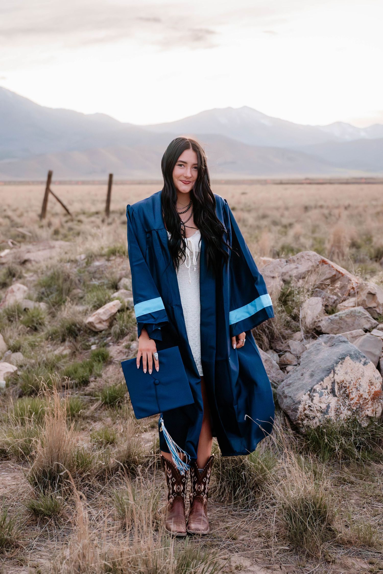 High school senior wearing a graduation gown with mountain views during an open field senior photography session in Utah County.