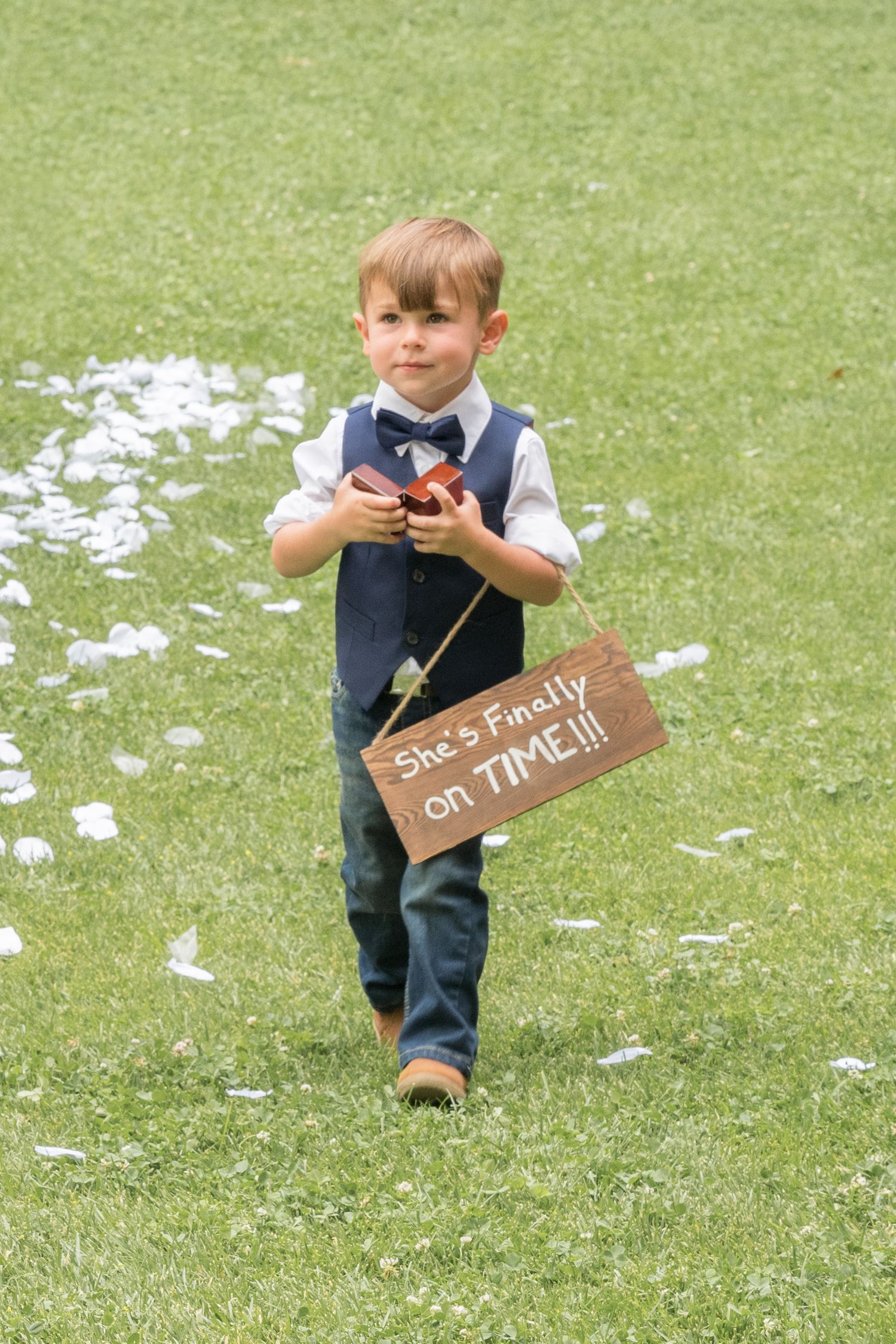 Young ring bearer walking down the aisle carrying a wedding sign during the ceremony.