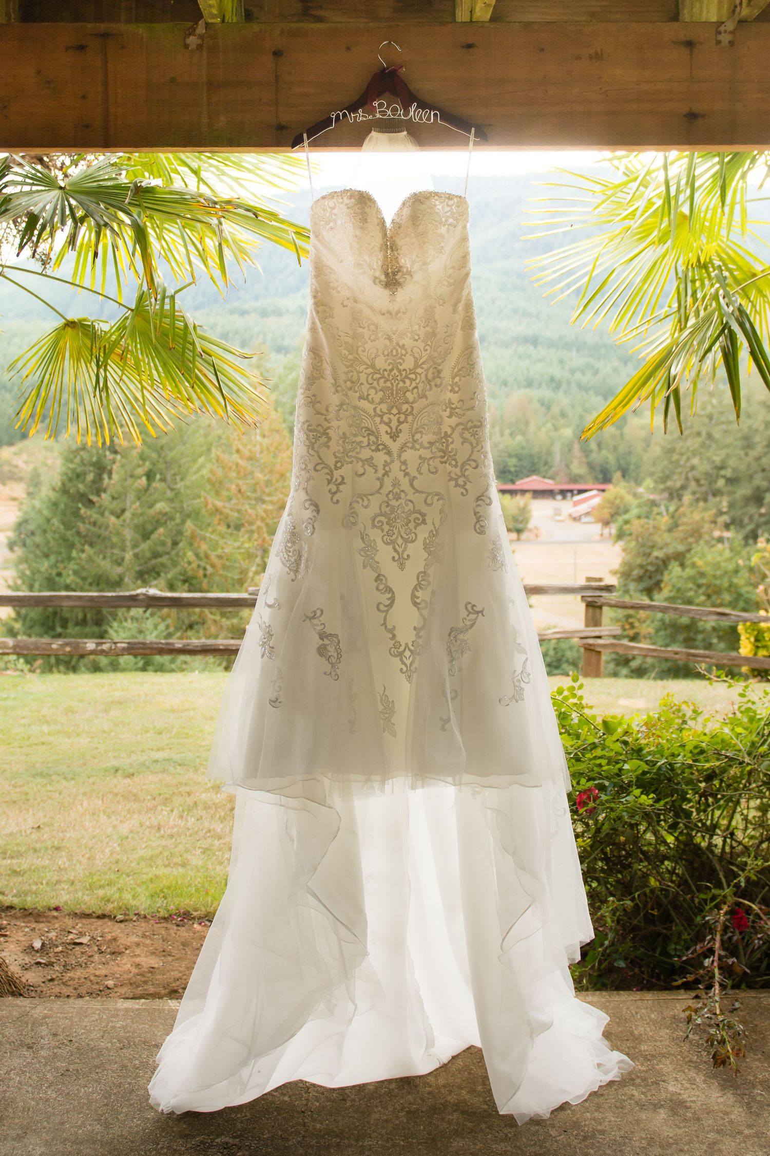 Elegant wedding dress hanging beneath a rustic wooden pavilion before the bride gets ready.