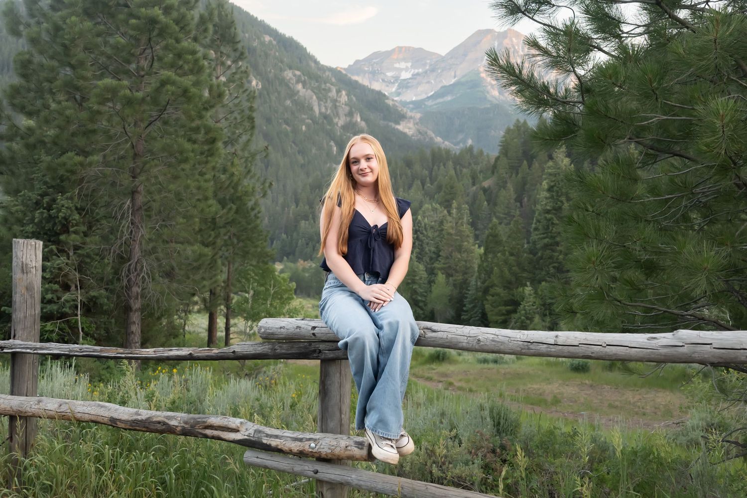 High school senior girl sitting on a rustic wooden fence with mountain views during an outdoor senior photography session in Utah.