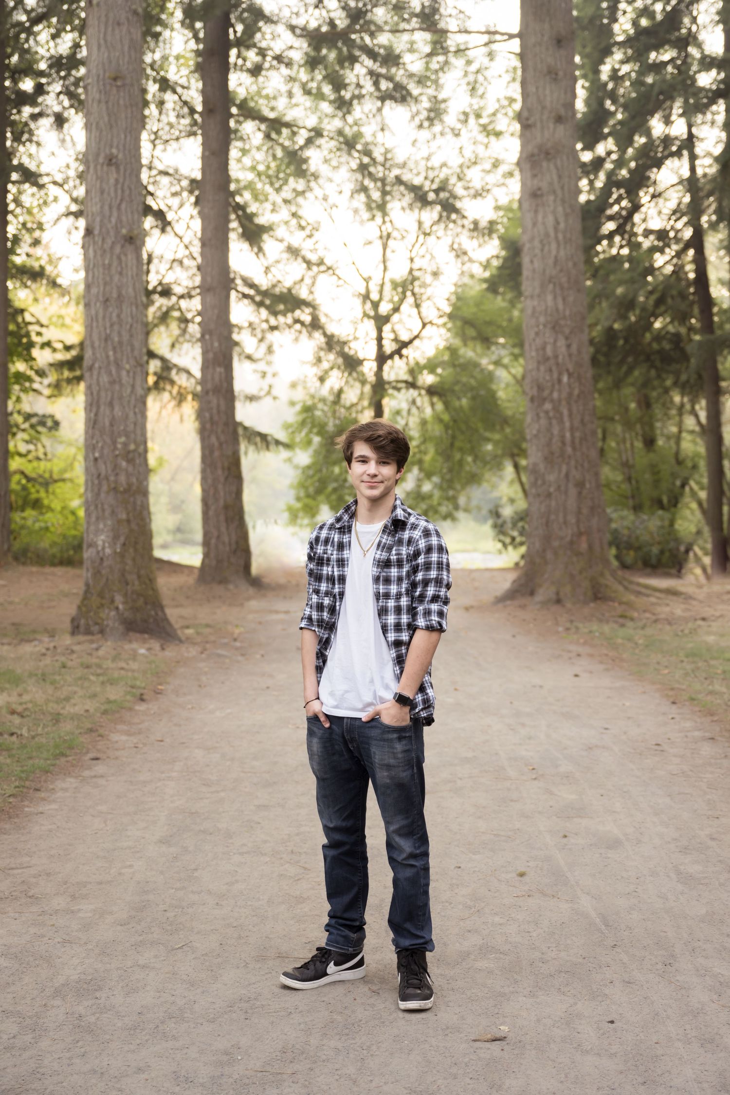 Natural light senior portrait featuring a young man surrounded by tall pine trees.