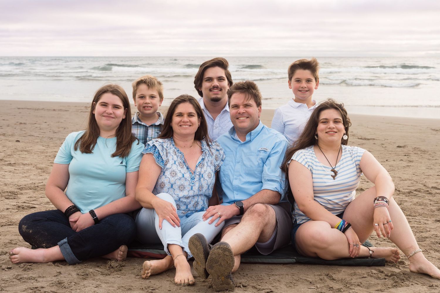 Family portrait on the beach capturing genuine smiles and beautiful coastal scenery at sunset.