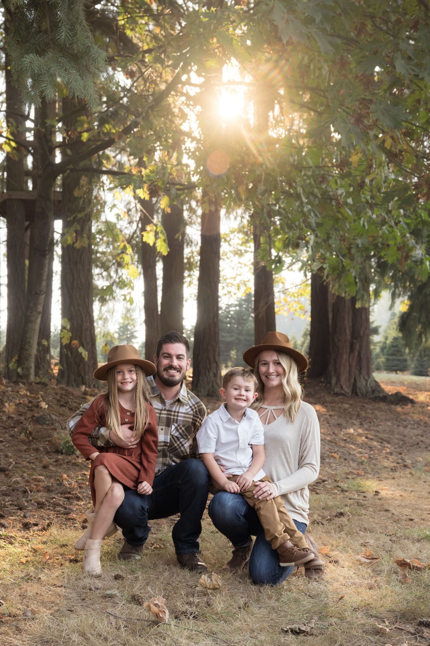 Family of four laughing together beneath tall trees during a warm fall family photography session in Washington.