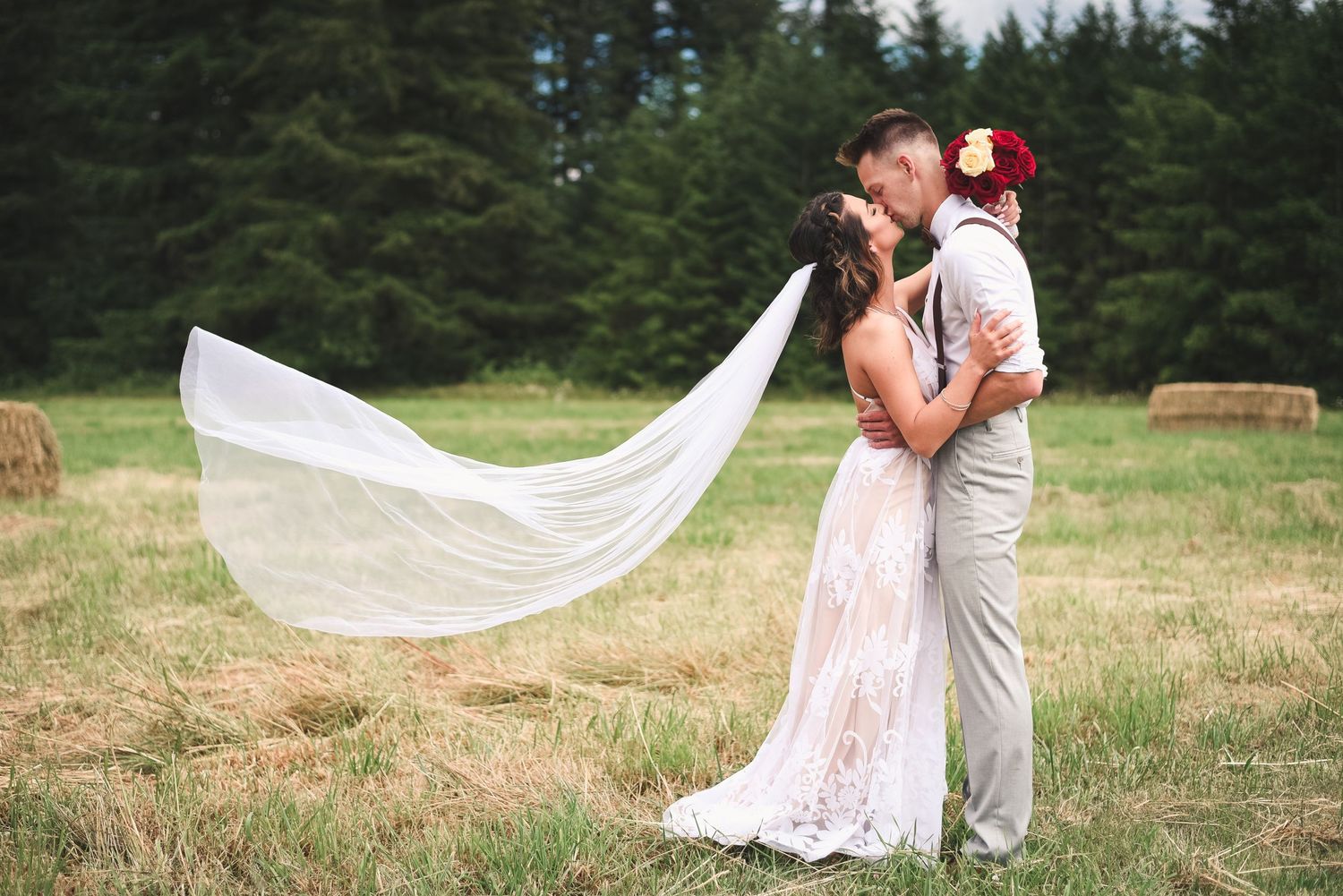 Bride and groom sharing a romantic kiss with the flowing wedding veil during an outdoor portrait session.