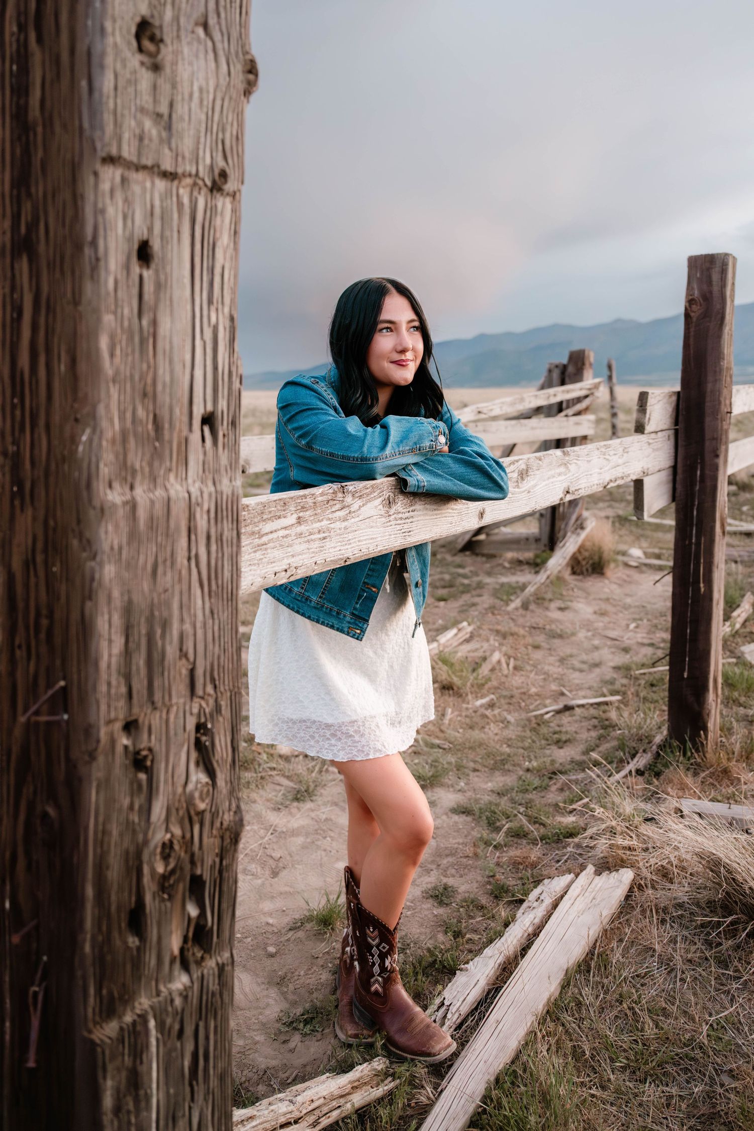 High school senior girl posing in a rustic wooden fence wearing a white dress during an outdoor senior portrait session in Utah.