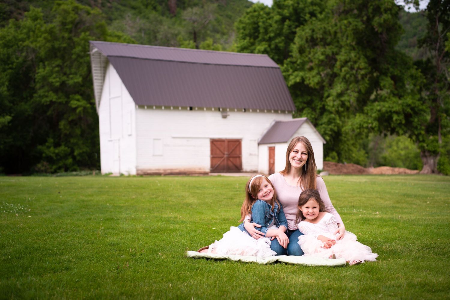 Mother and her two children sitting together in front of a white barn during a relaxed outdoor family photography session in Utah.