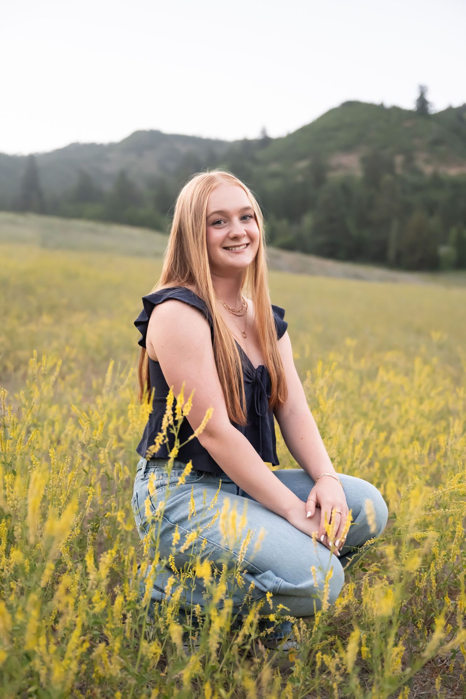 Strawberry blonde high school senior sitting in a field of wildflowers during a golden hour senior photography session in Utah County.