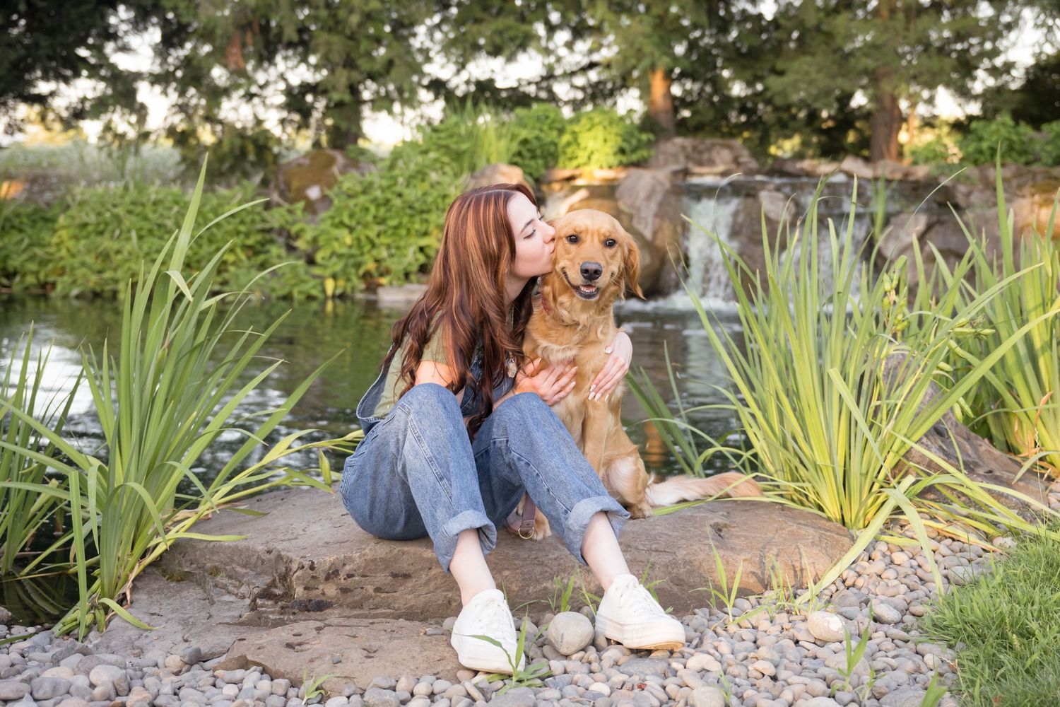 High school senior girl sitting beside a pond with her golden retriever during a personalized outdoor senior photography session in Utah.