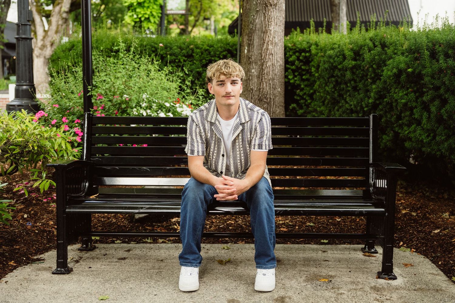 High school senior boy sitting on a park bench during a relaxed outdoor senior portrait session with natural light in Camas, WA.