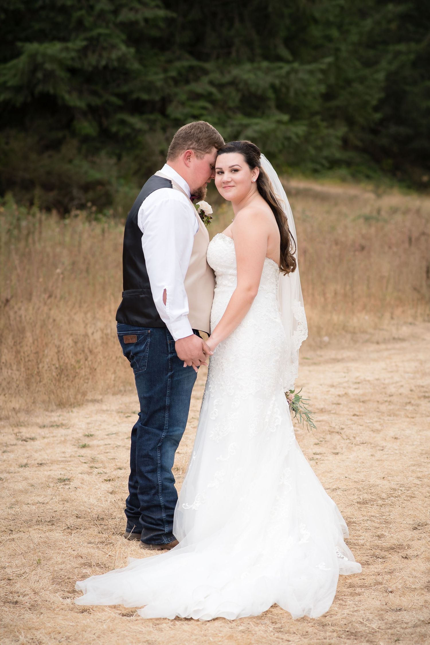 Bride and groom sharing a romantic embrace while bride looks at camera during an outdoor wedding portrait session.