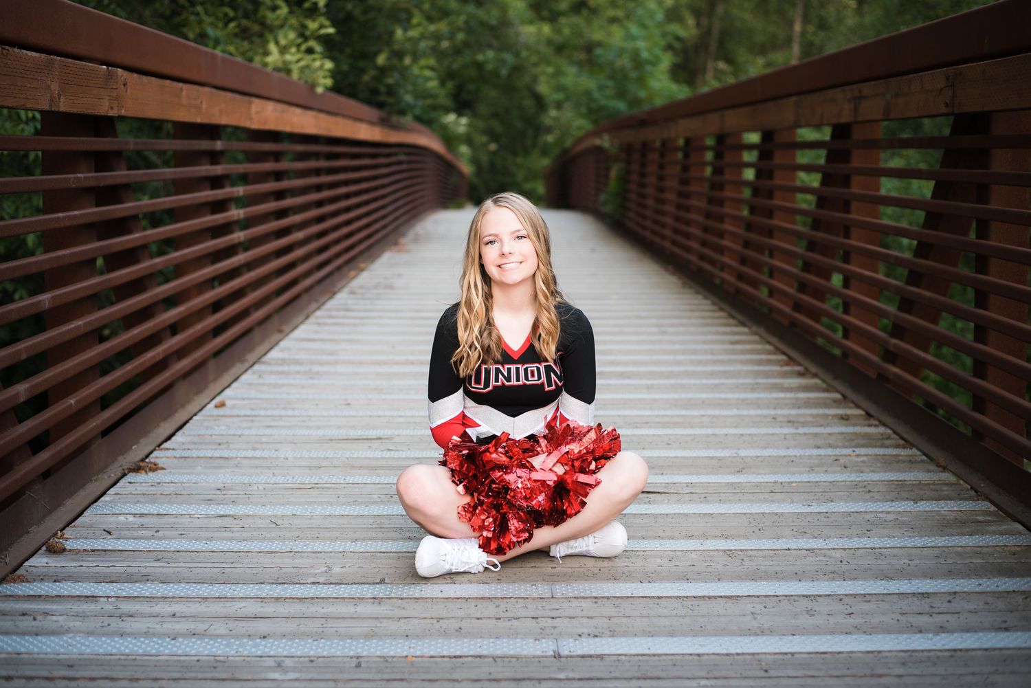 Natural light senior portrait featuring a young woman on a scenic pedestrian bridge.