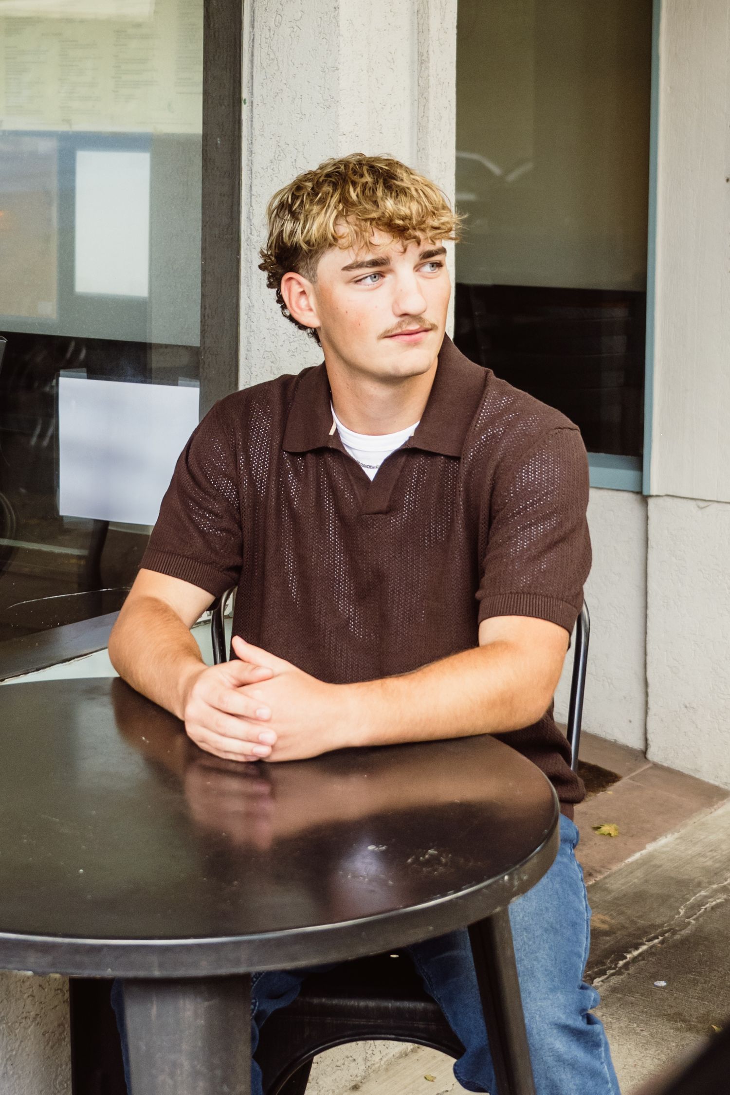 High school senior boy sitting at an outdoor café table during a modern lifestyle senior portrait session in Utah.