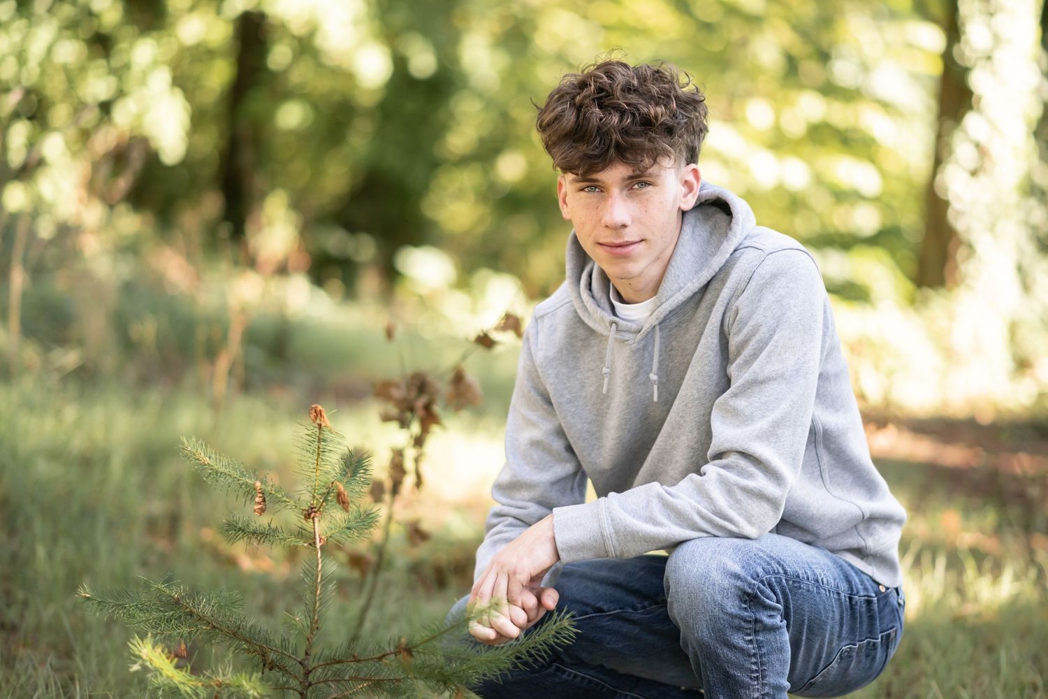 High school senior boy crouching in a sunlit field during a relaxed natural light senior portrait session in Utah.