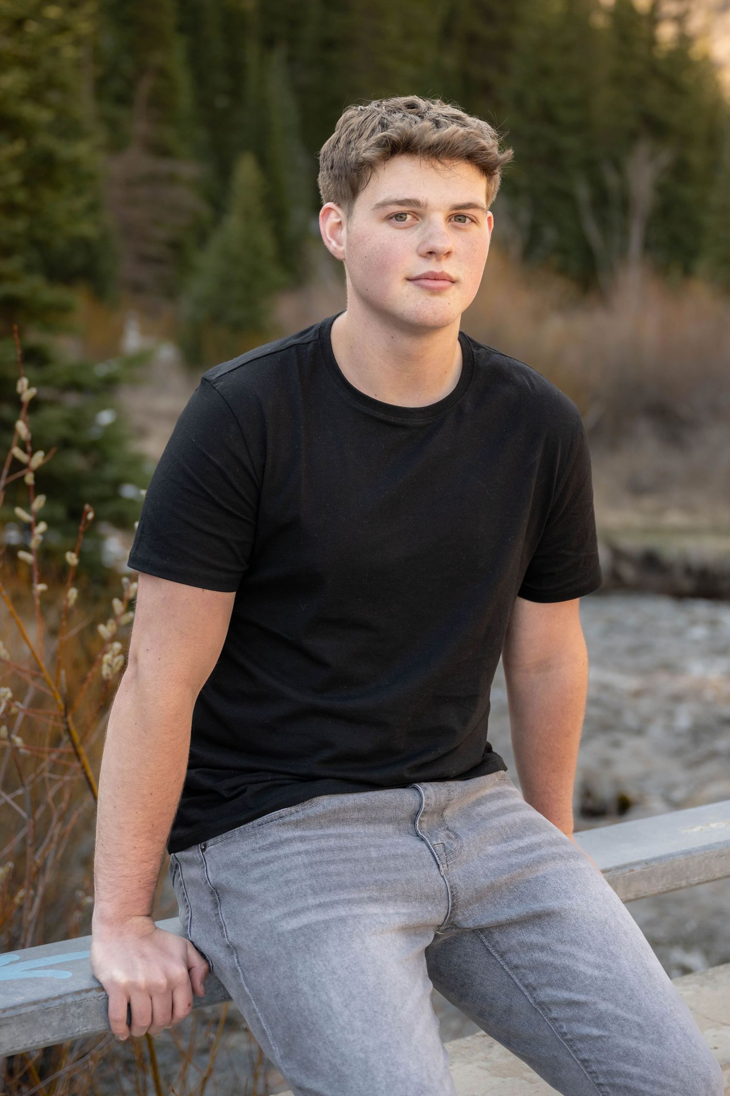 High school senior boy sitting outdoors on a stone ledge during a casual natural light senior photography session in Utah.