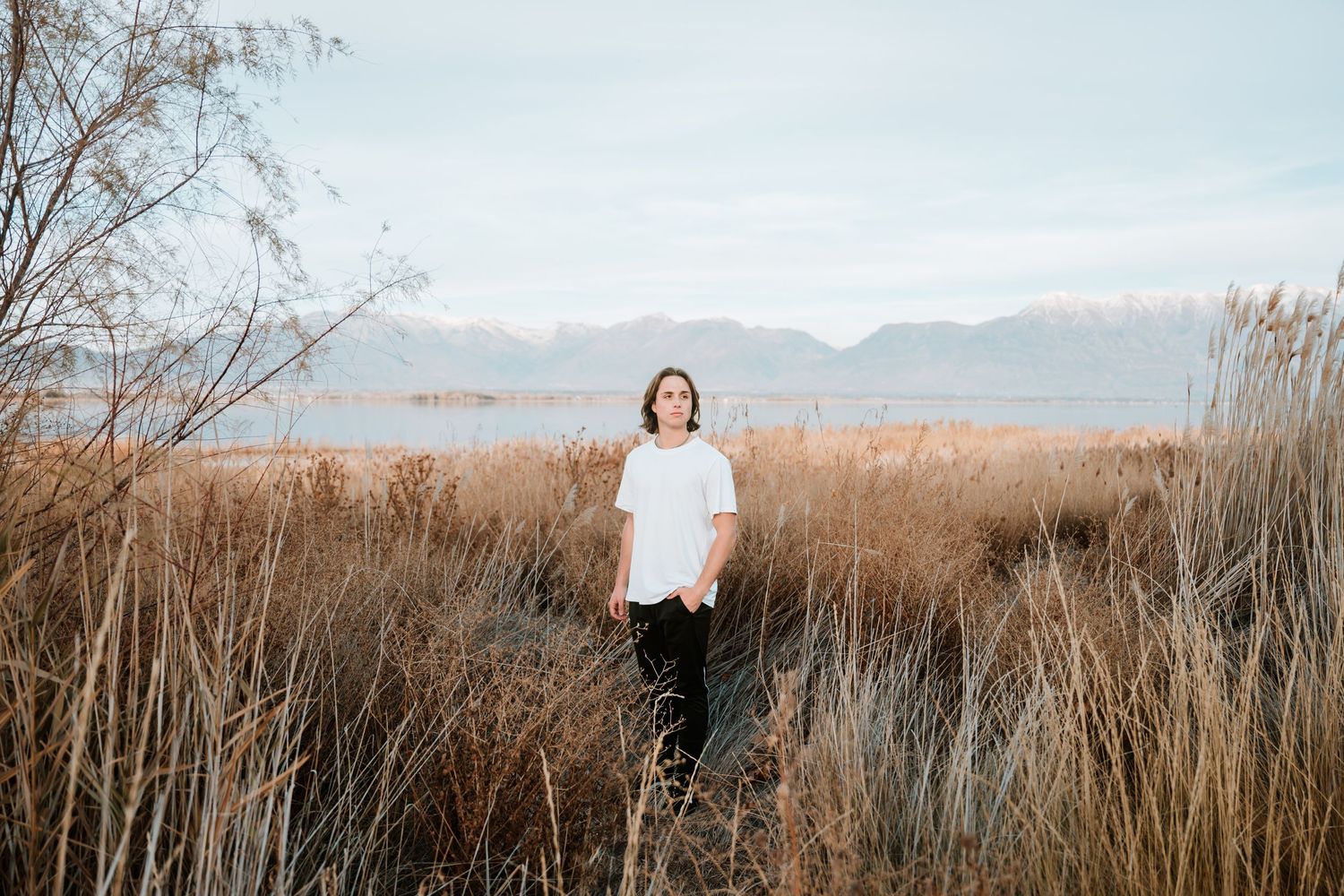 Natural light senior portrait featuring a young man surrounded by tall grasses with mountain views.