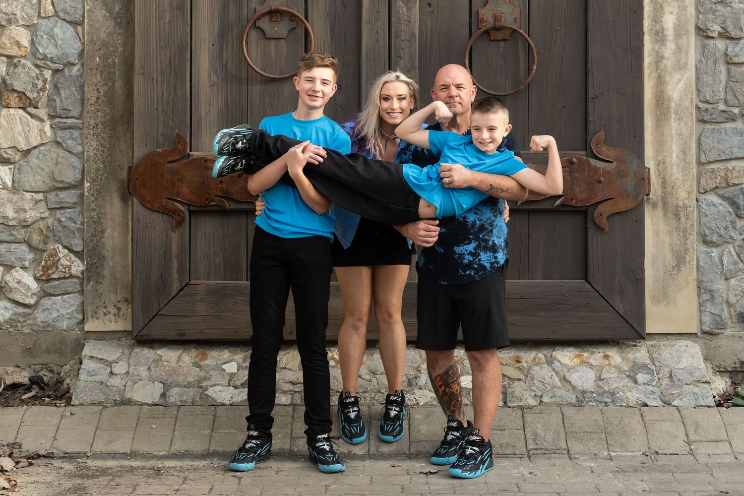 Family of four smiling together outside rustic wooden doors during an outdoor family photography session in Dallas, TX.