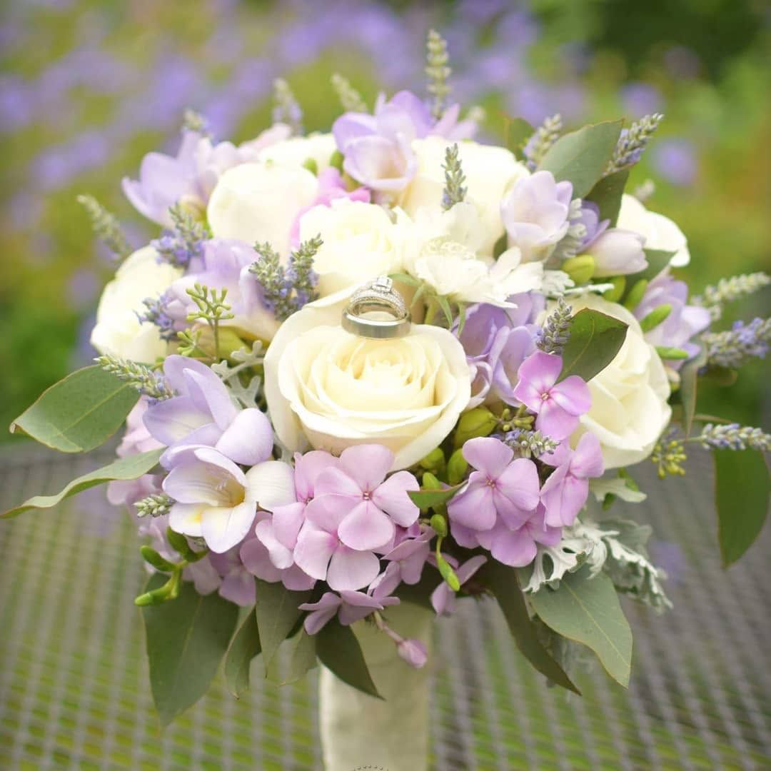 Close-up of a romantic wedding bouquet featuring white roses, lavender blooms, and greenery.