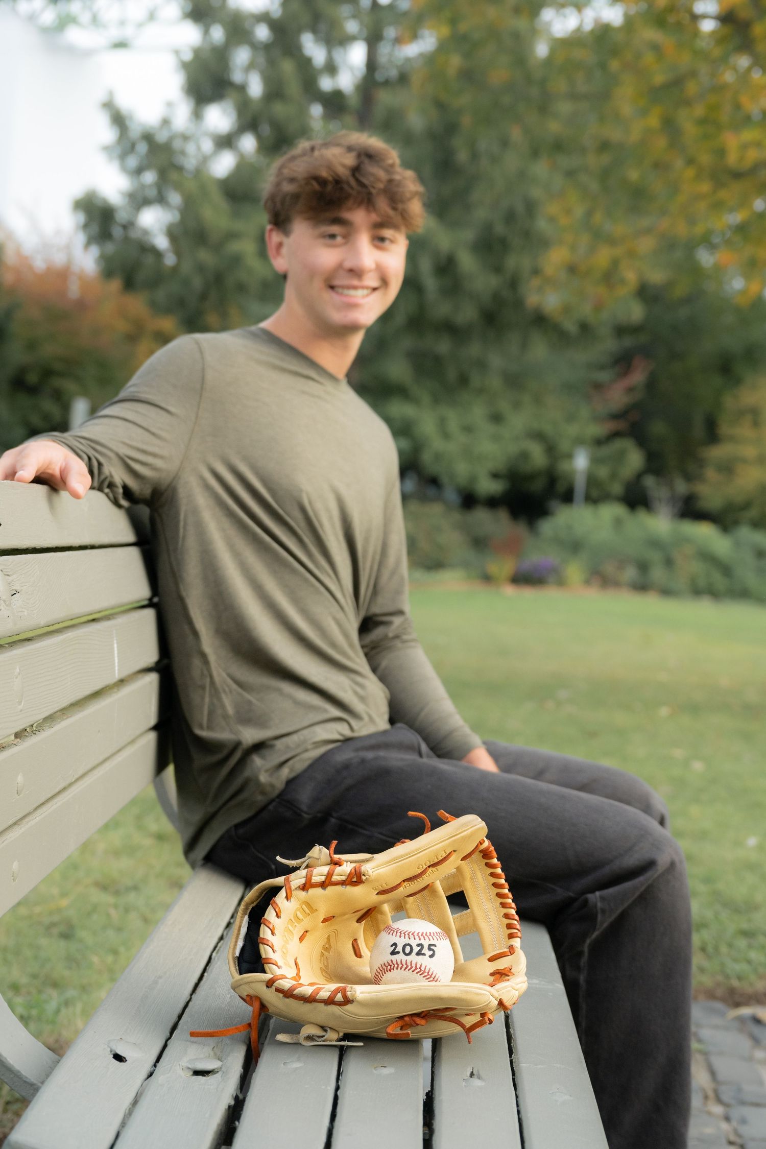High school senior boy sitting on a park bench during a relaxed outdoor senior portrait session with natural light in Washington.