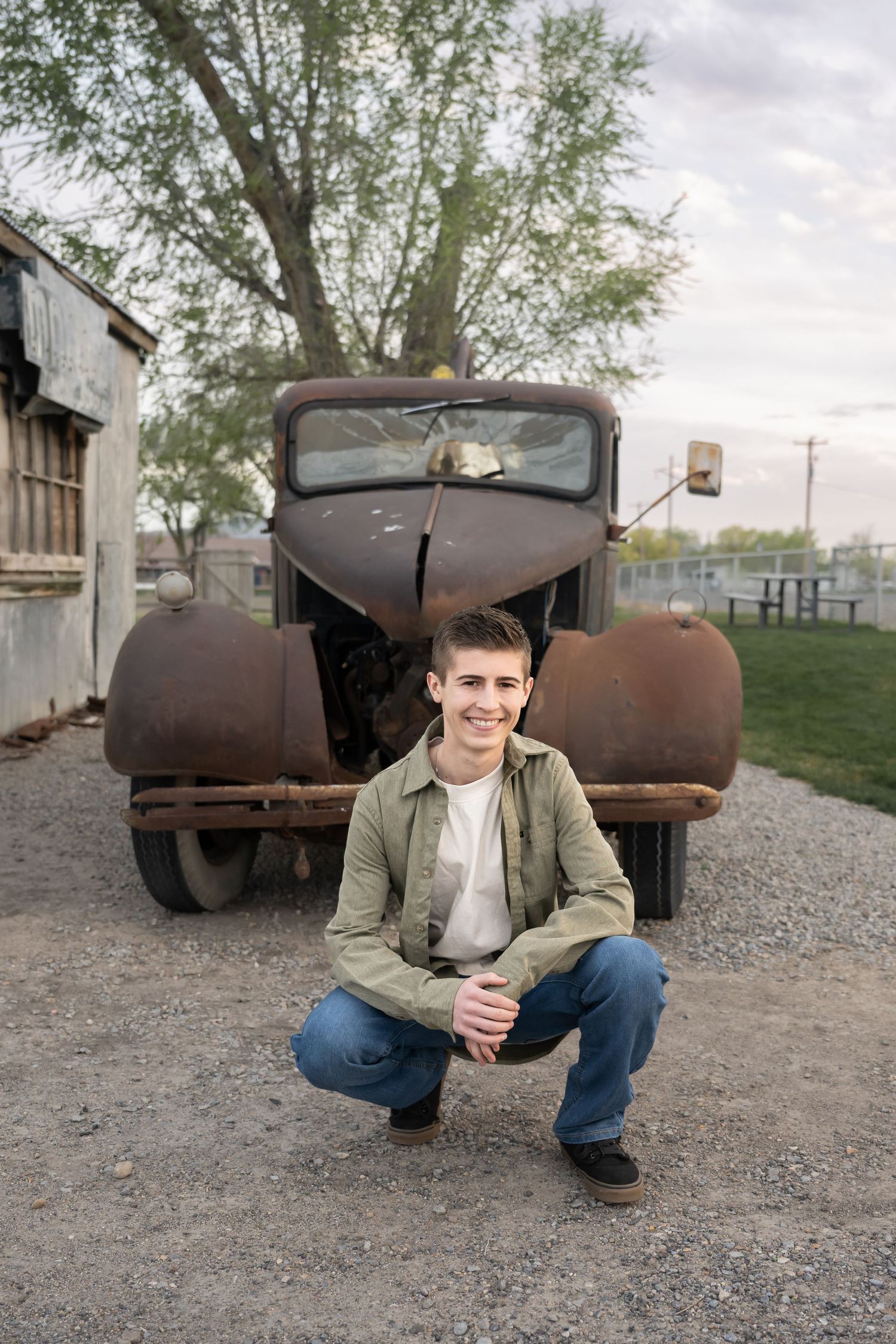 Natural light senior portrait featuring a young man in a rustic vintage setting with truck.