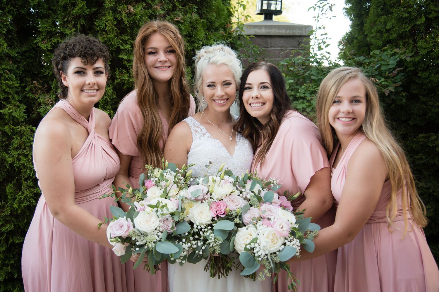 Bride and bridesmaids smiling together while holding a beautiful bouquet during wedding portraits.