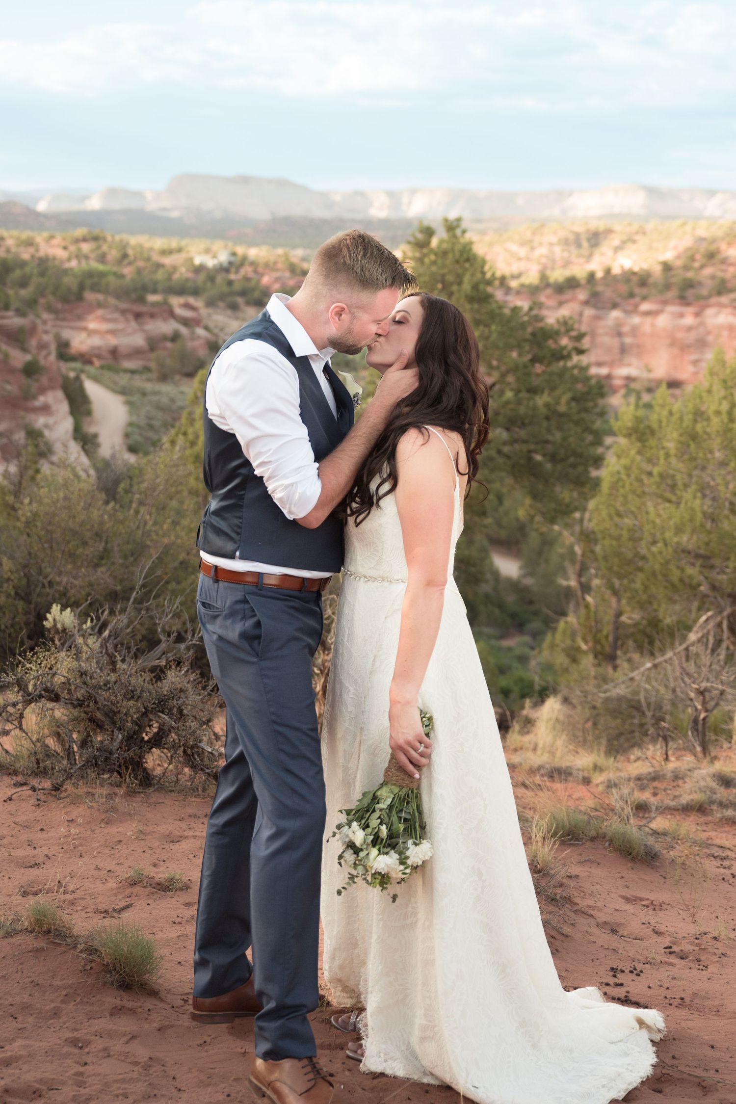 Bride and groom embracing during romantic wedding portraits with scenic red rock views.