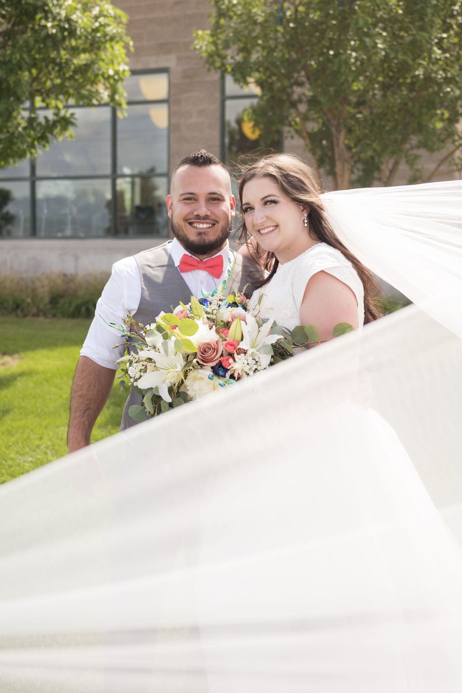 Bride and groom sharing a joyful wedding portrait beneath the flowing bridal veil.