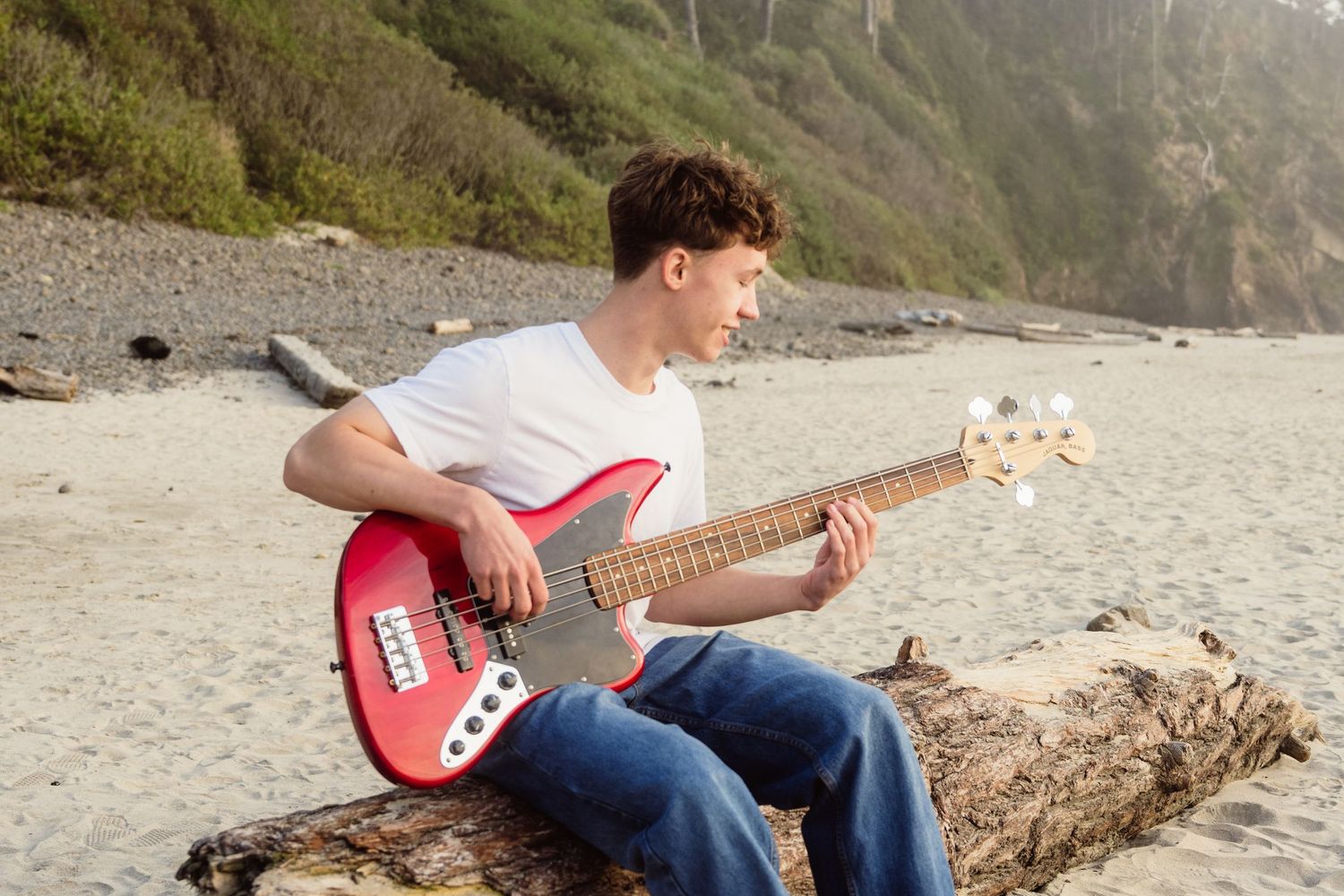 High school senior boy playing a red electric guitar on a sandy beach during a creative outdoor senior photography session.