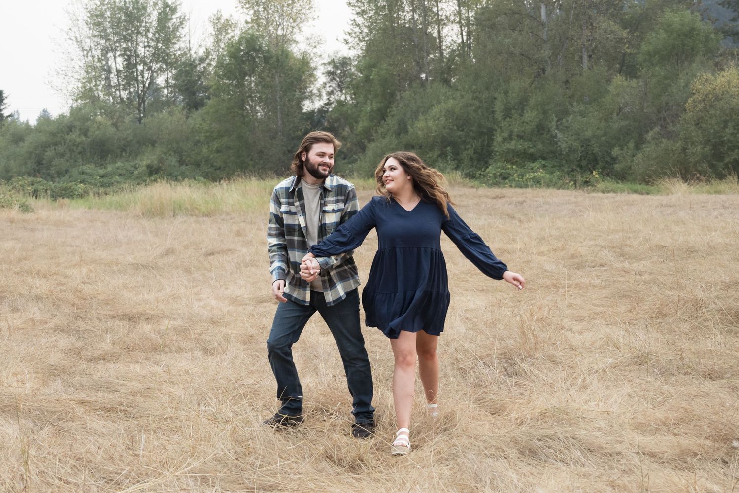 Couple laughing and running together through an open field during a fun engagement session.